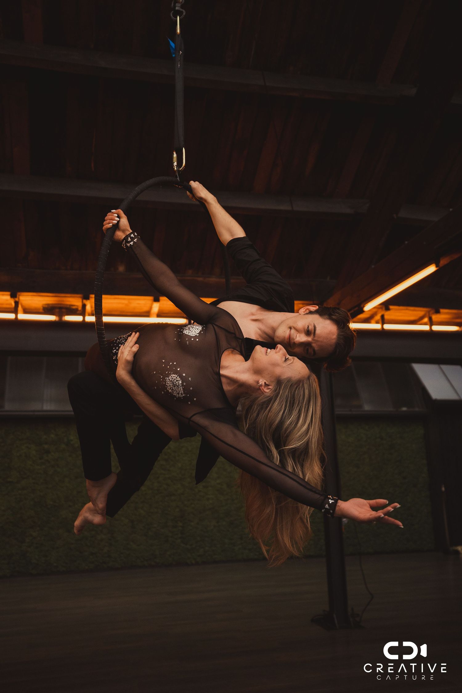 Dancer performing an elegant aerial silk routine against dramatic lighting in a studio space.