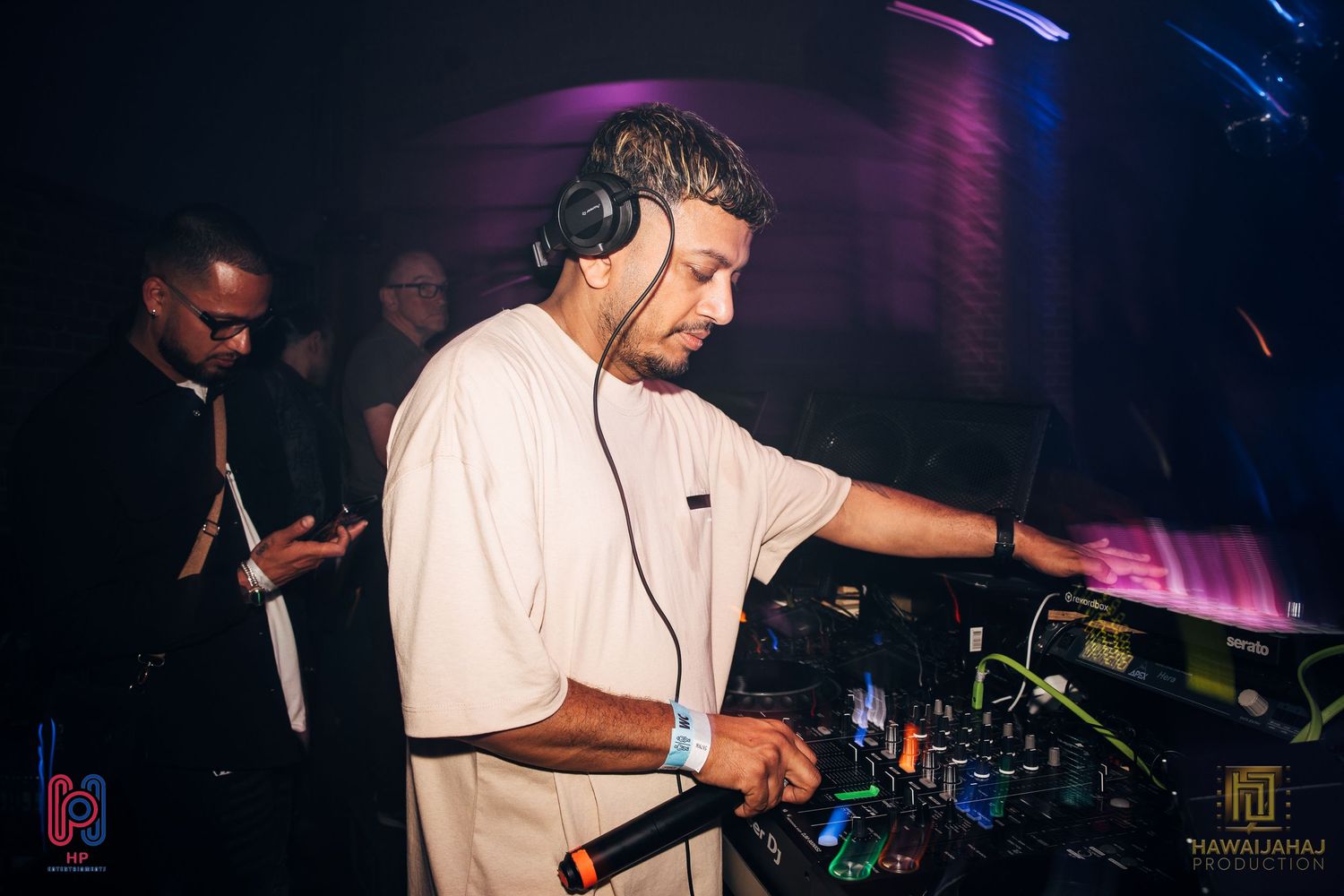 DJ performing at mixing console under purple stage lights in nightclub atmosphere.