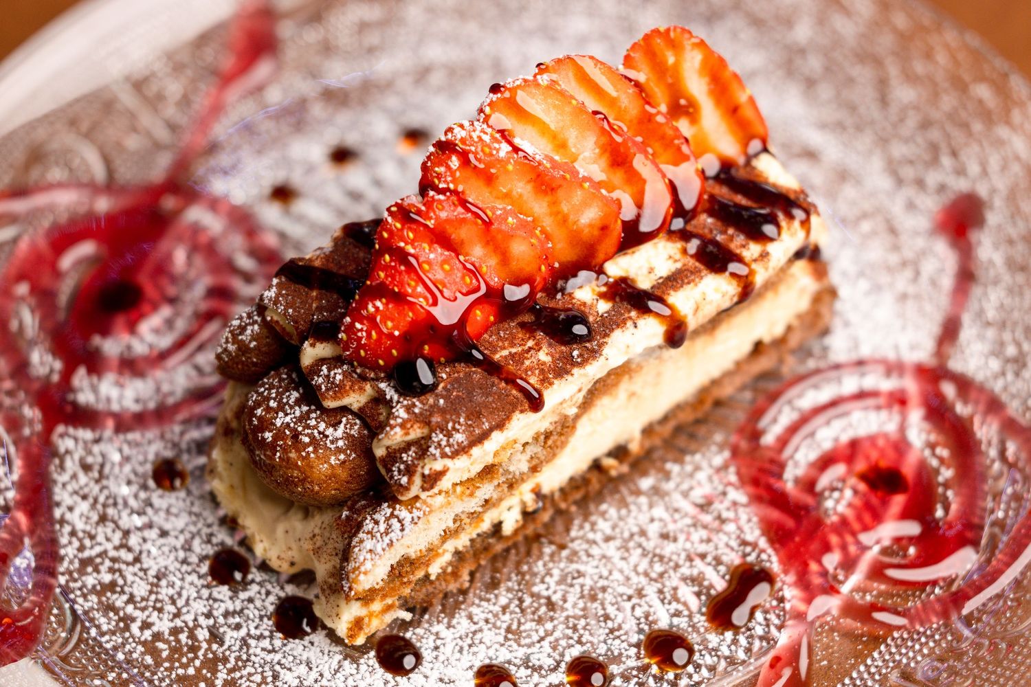 Decadent chocolate dessert topped with fresh strawberries and powdered sugar on an elegant plate with raspberry sauce.