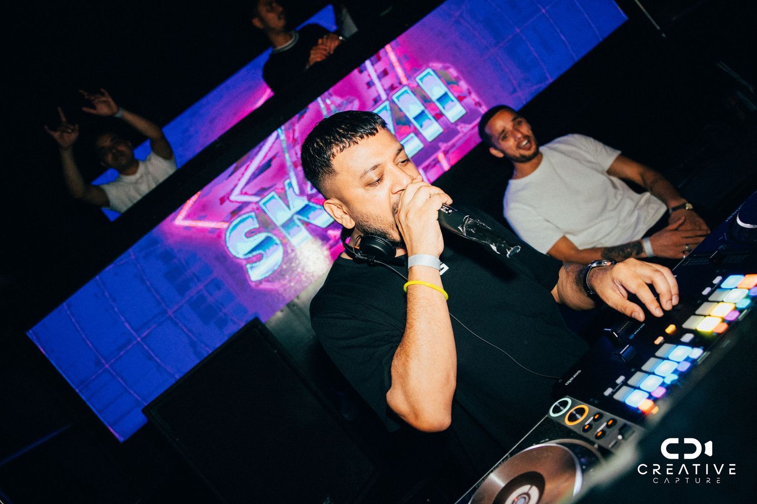 DJ performing at nightclub with electronic equipment and blue lighting effects.