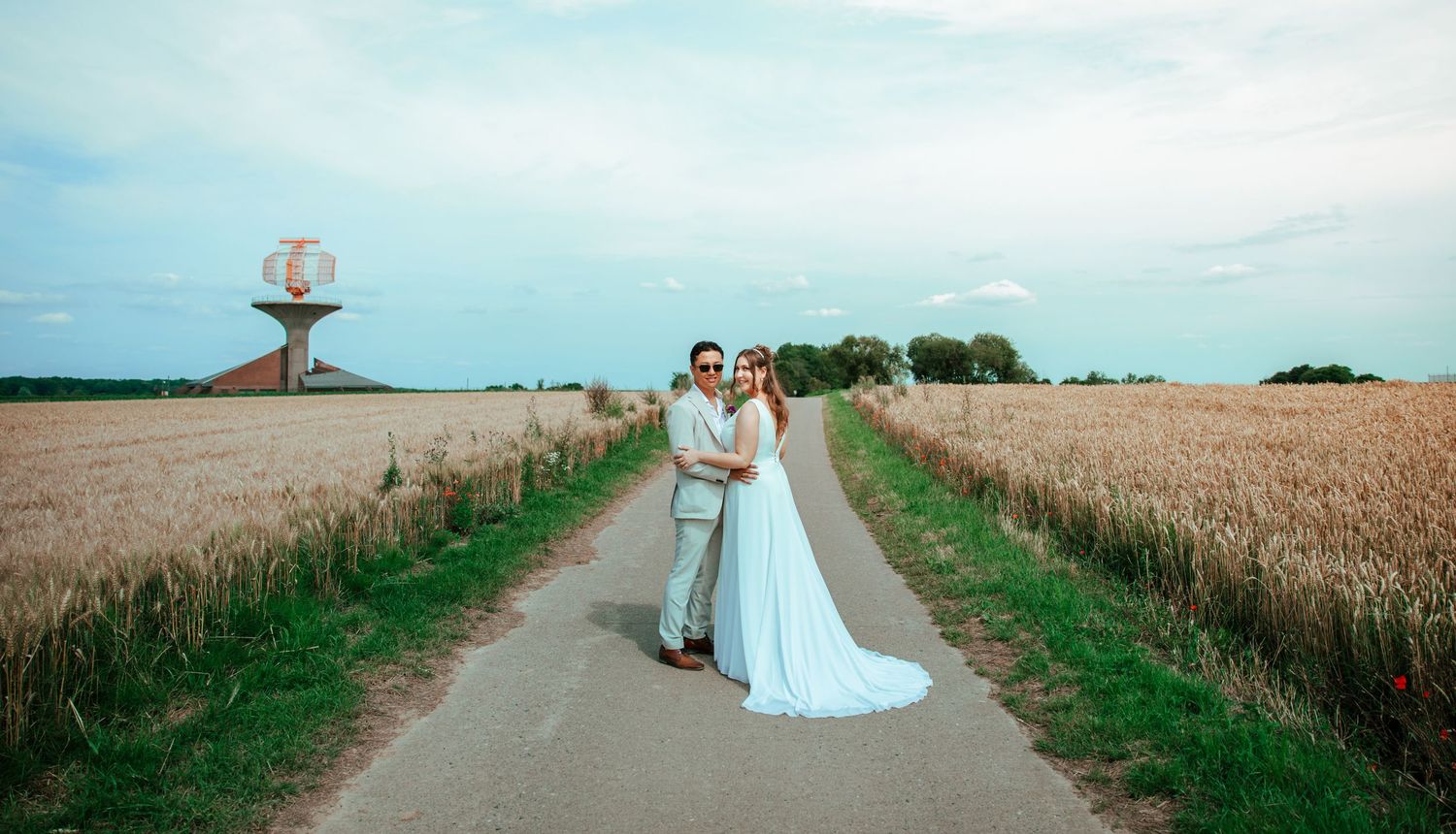 Wedding couple walking along countryside path with wheat fields and blue sky.