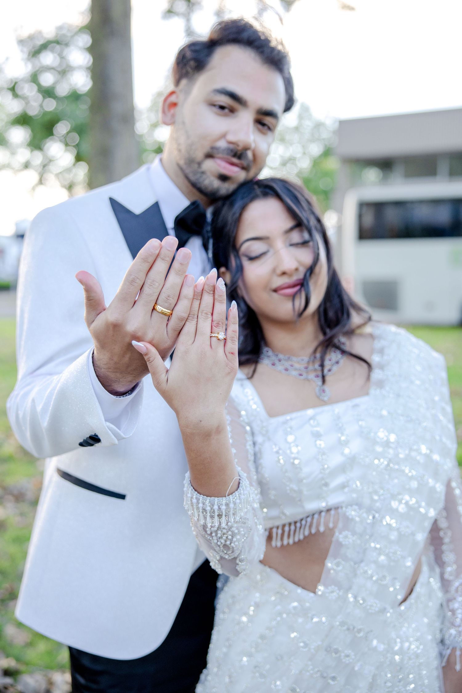 Newlyweds showing off their wedding rings while wearing elegant white attire.
