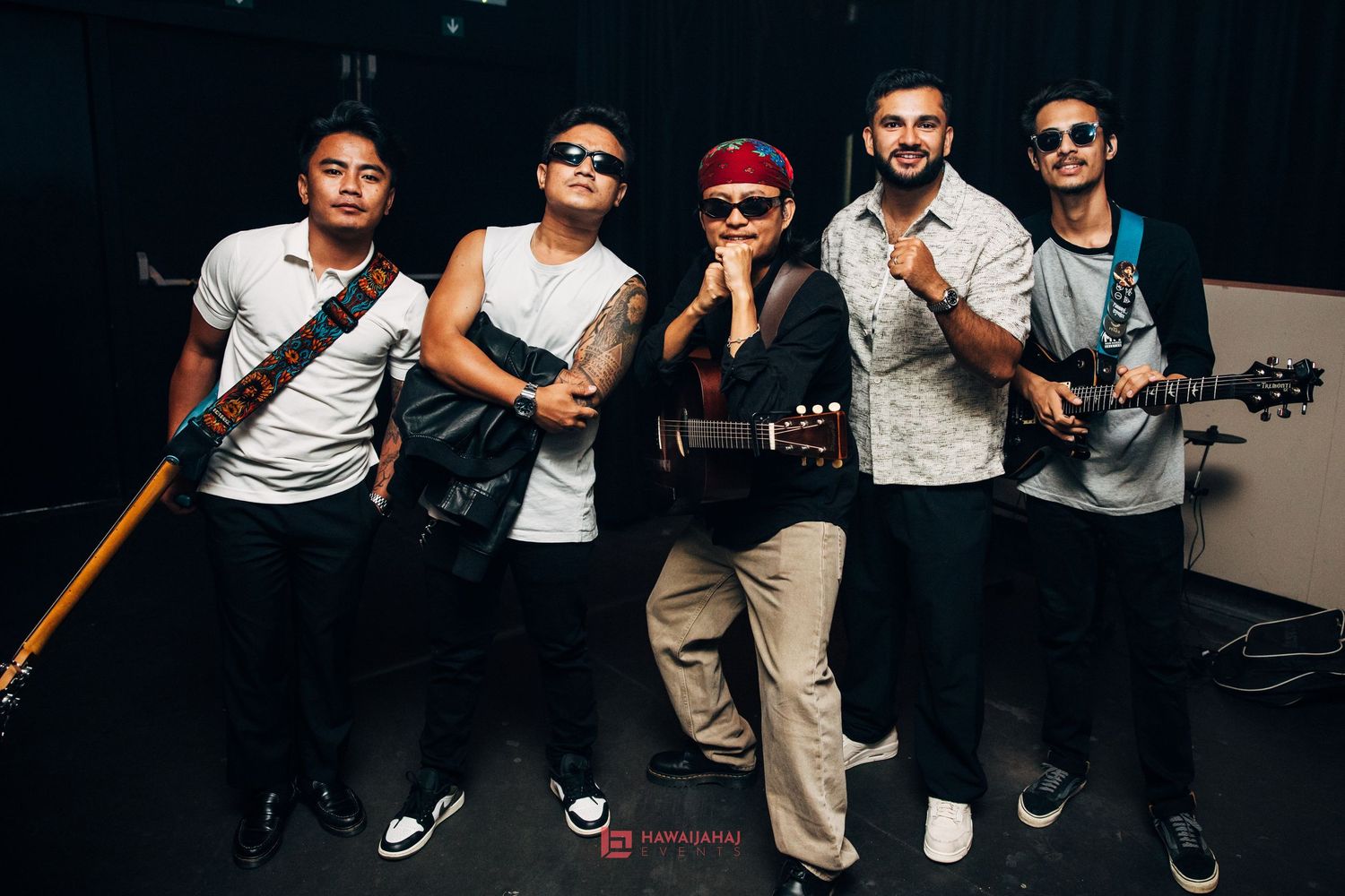 Band members posing with musical instruments against dark background.