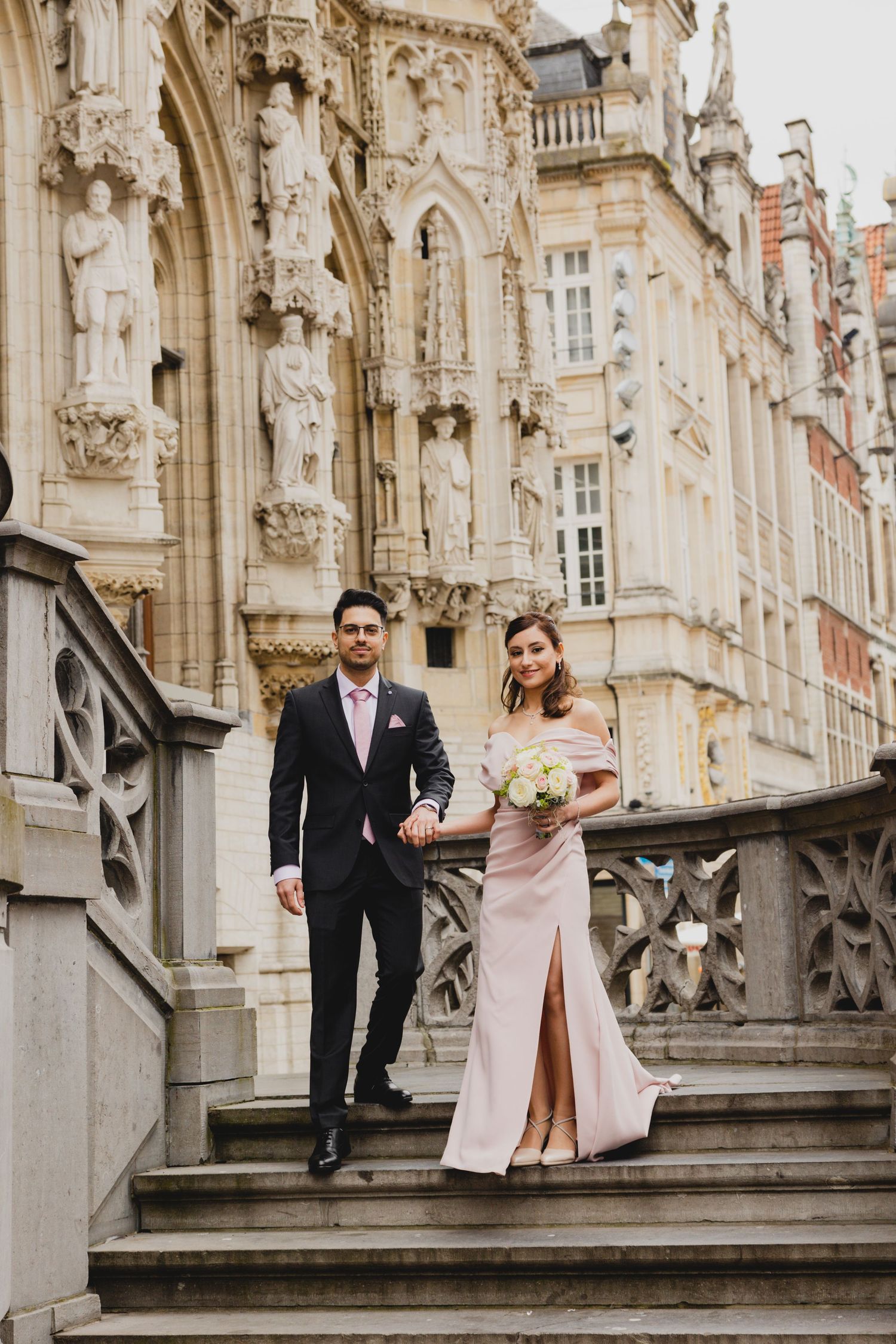 Couple poses on ornate stone staircase at historic building for wedding photos.