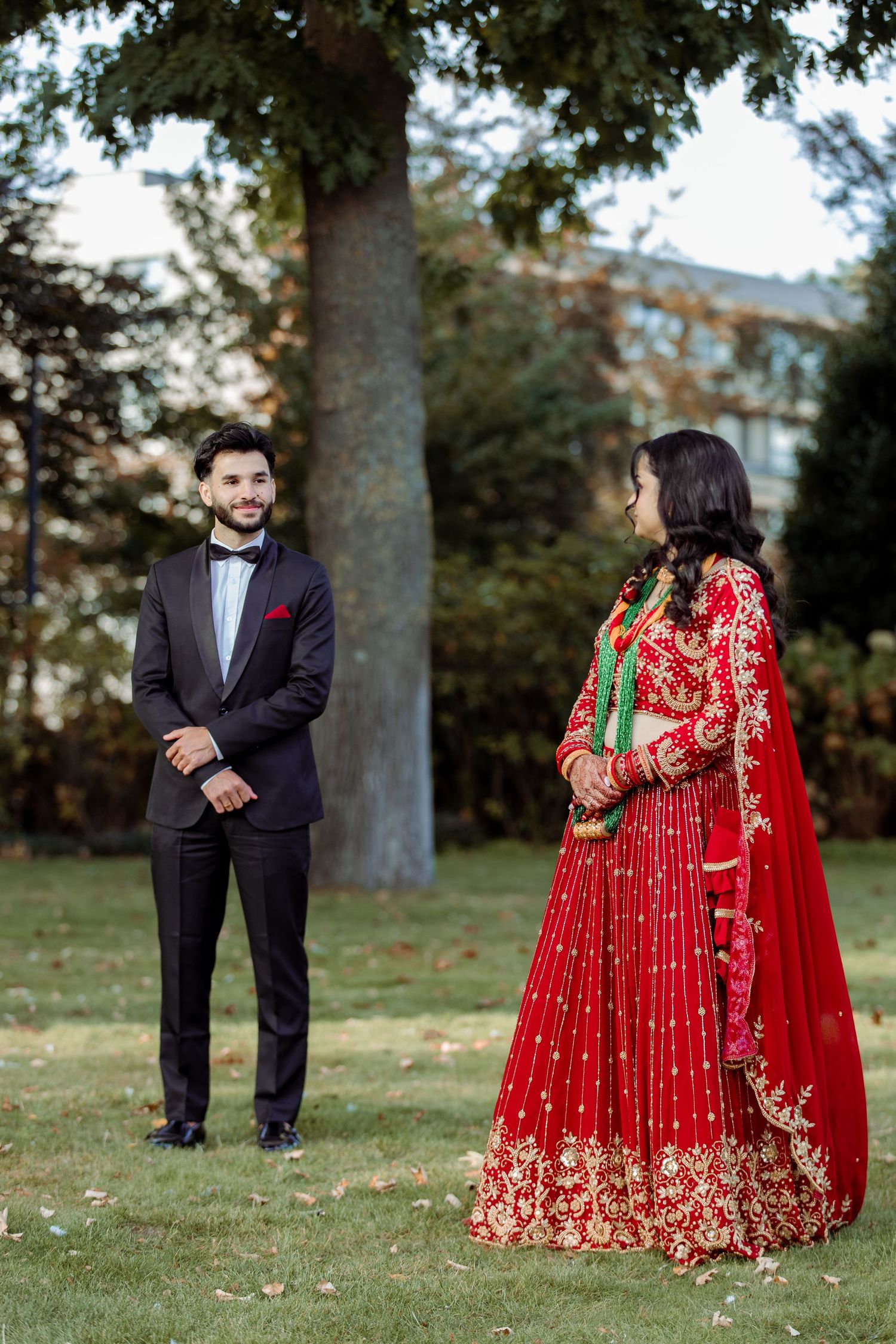 Wedding couple in traditional red and black attire pose in a park setting.