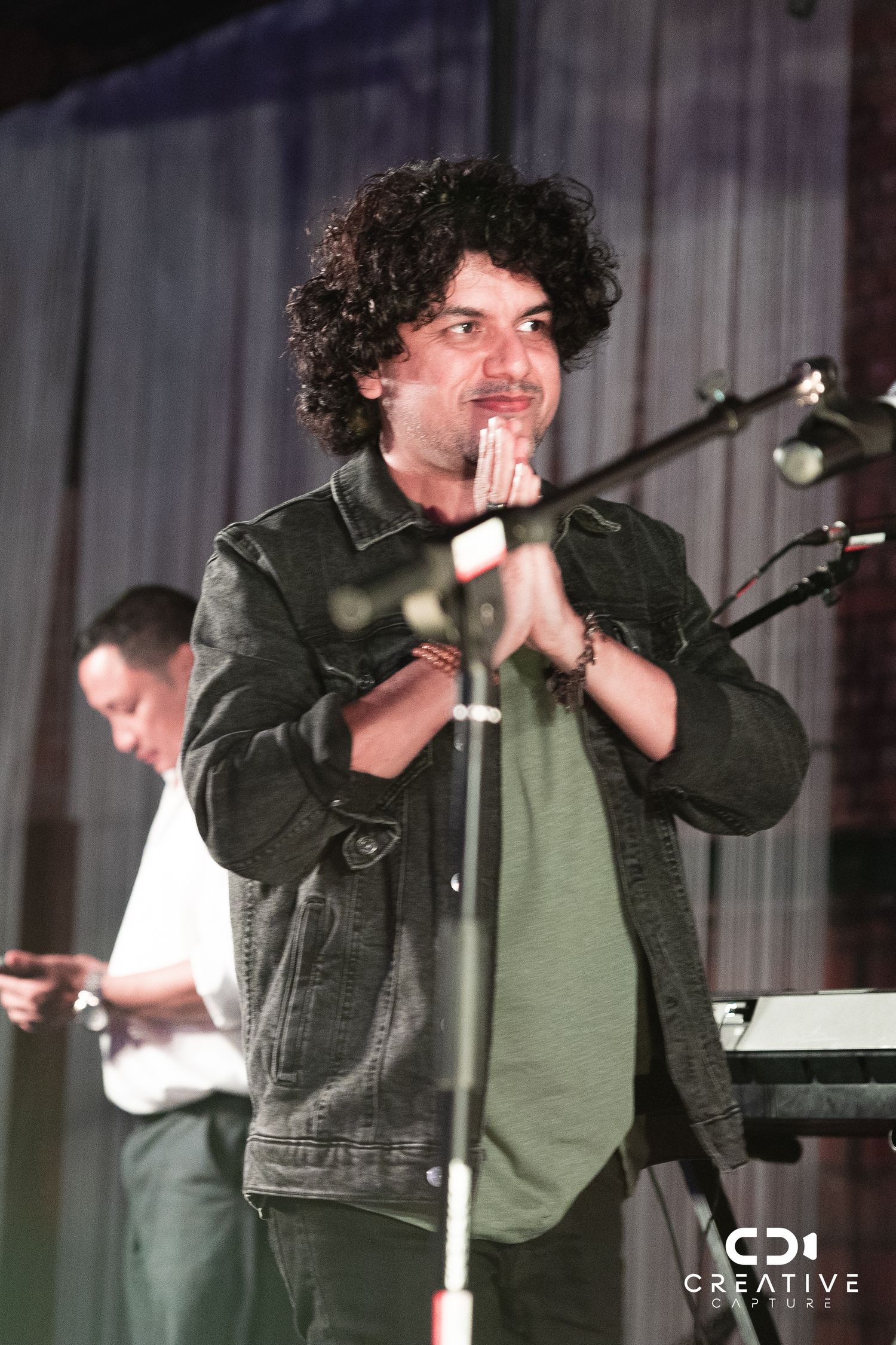 Concert performer in denim jacket holds microphone while standing at stage microphone stand.