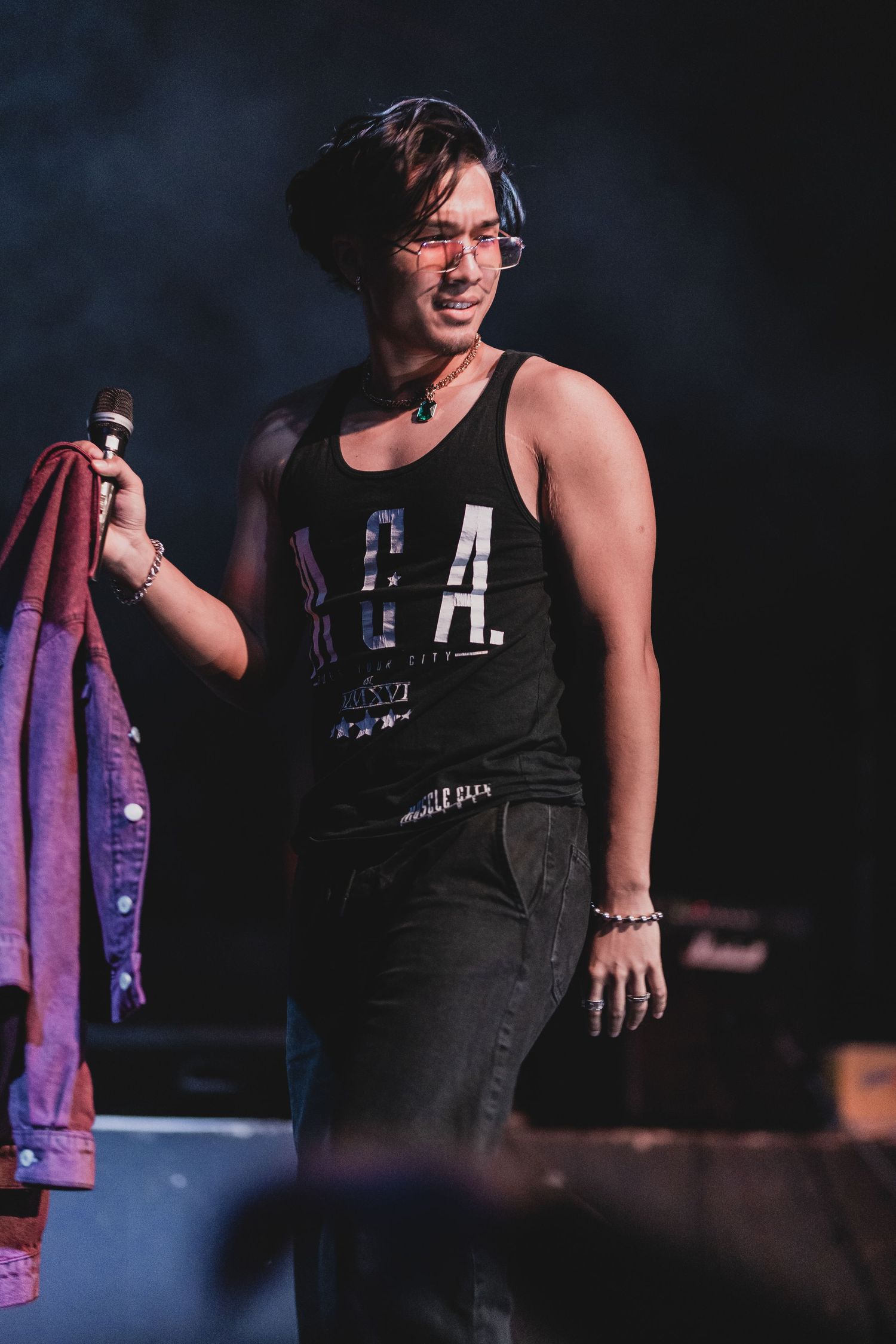 Performer in a black tank top with LA text performing on stage with atmospheric lighting.