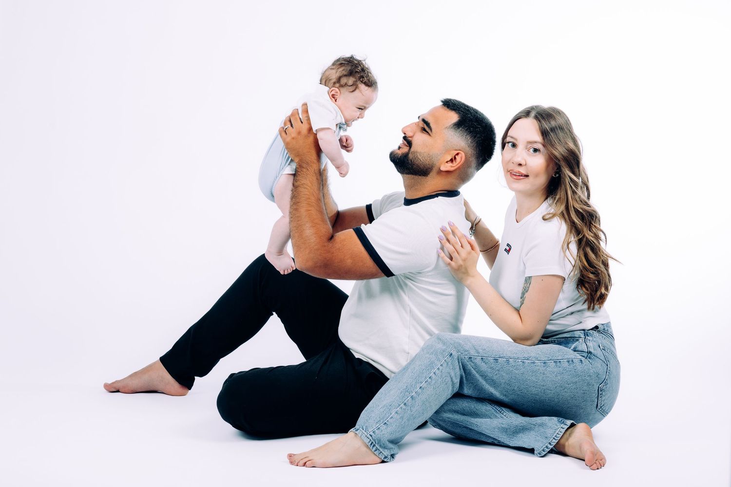 Family lying down and playing together on white studio floor in casual attire.