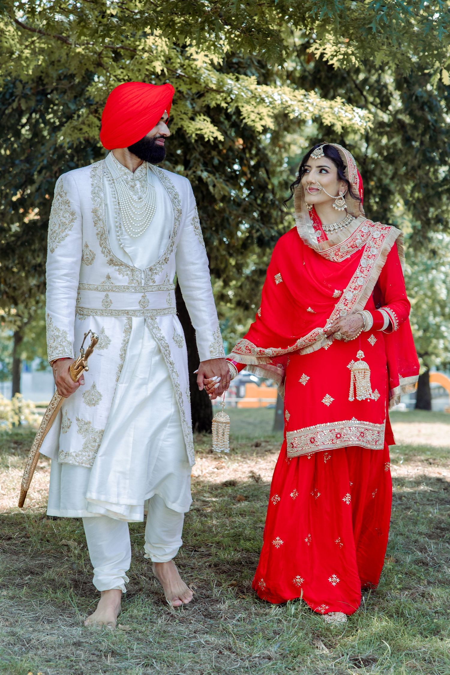 Traditional Sikh wedding couple in white and red attire posing outdoors.