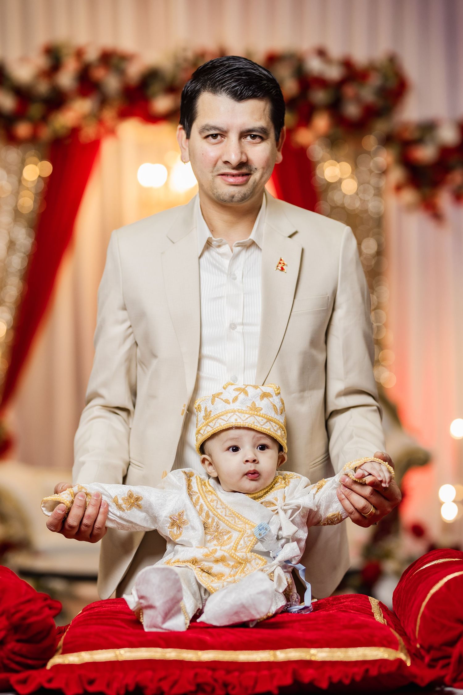 Family portrait session with baby in crown on red velvet backdrop with floral decorations.