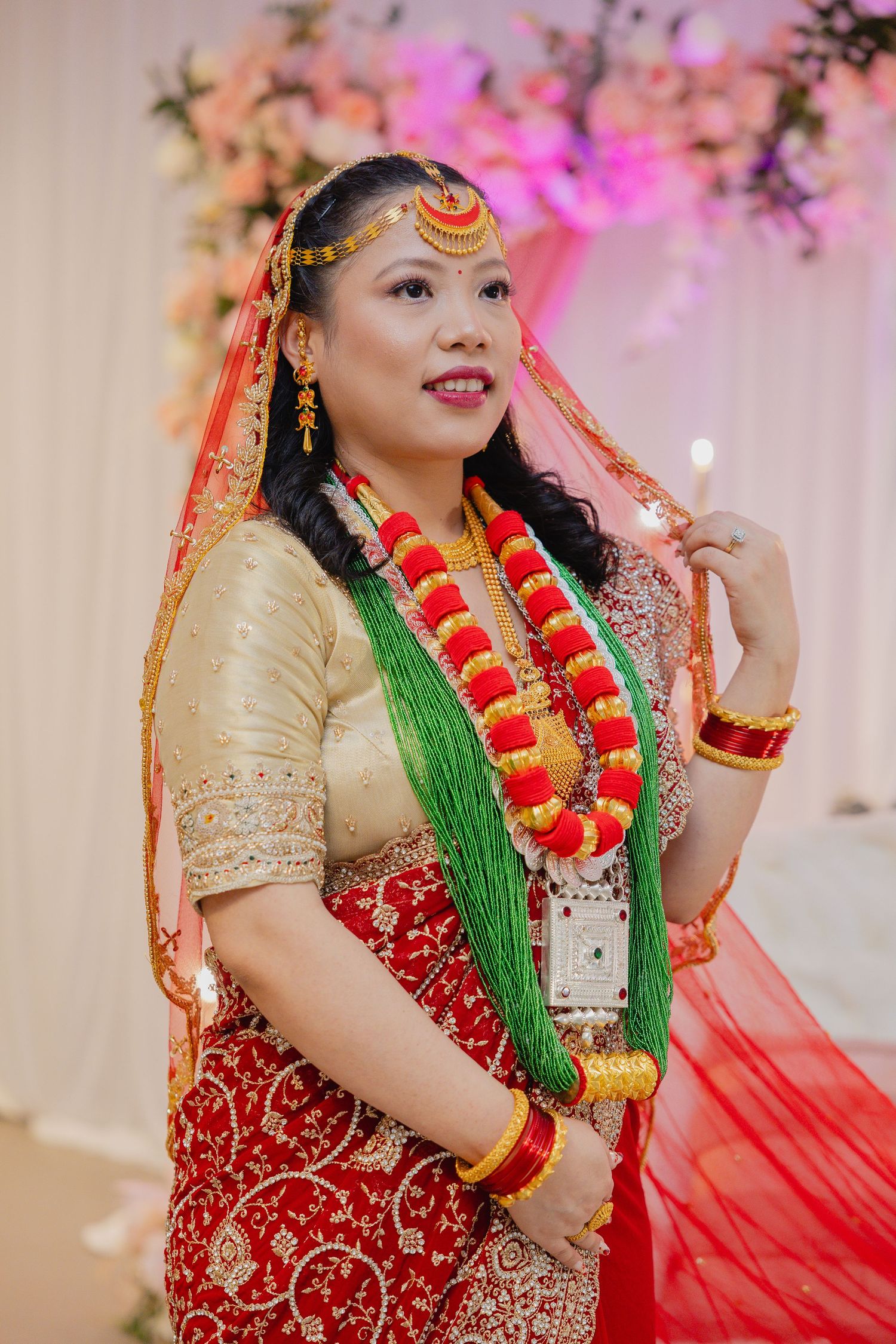 Traditional South Asian bride wearing red and gold attire with ornate jewelry and green accents.
