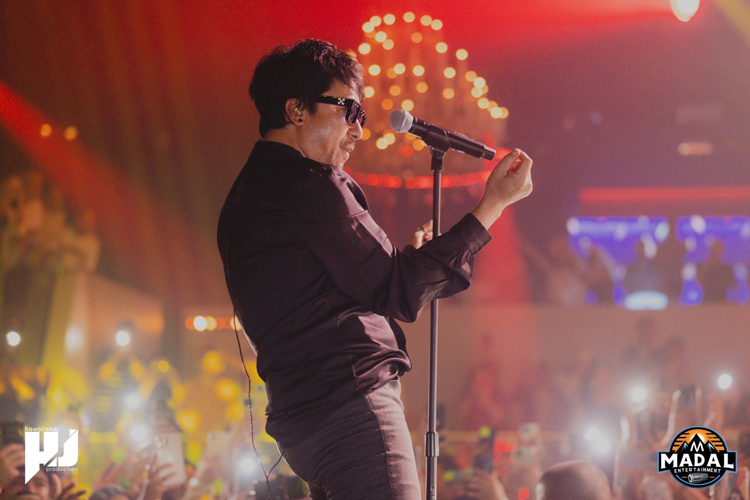 Singer performing passionately at microphone stand with red ambient lighting in background.