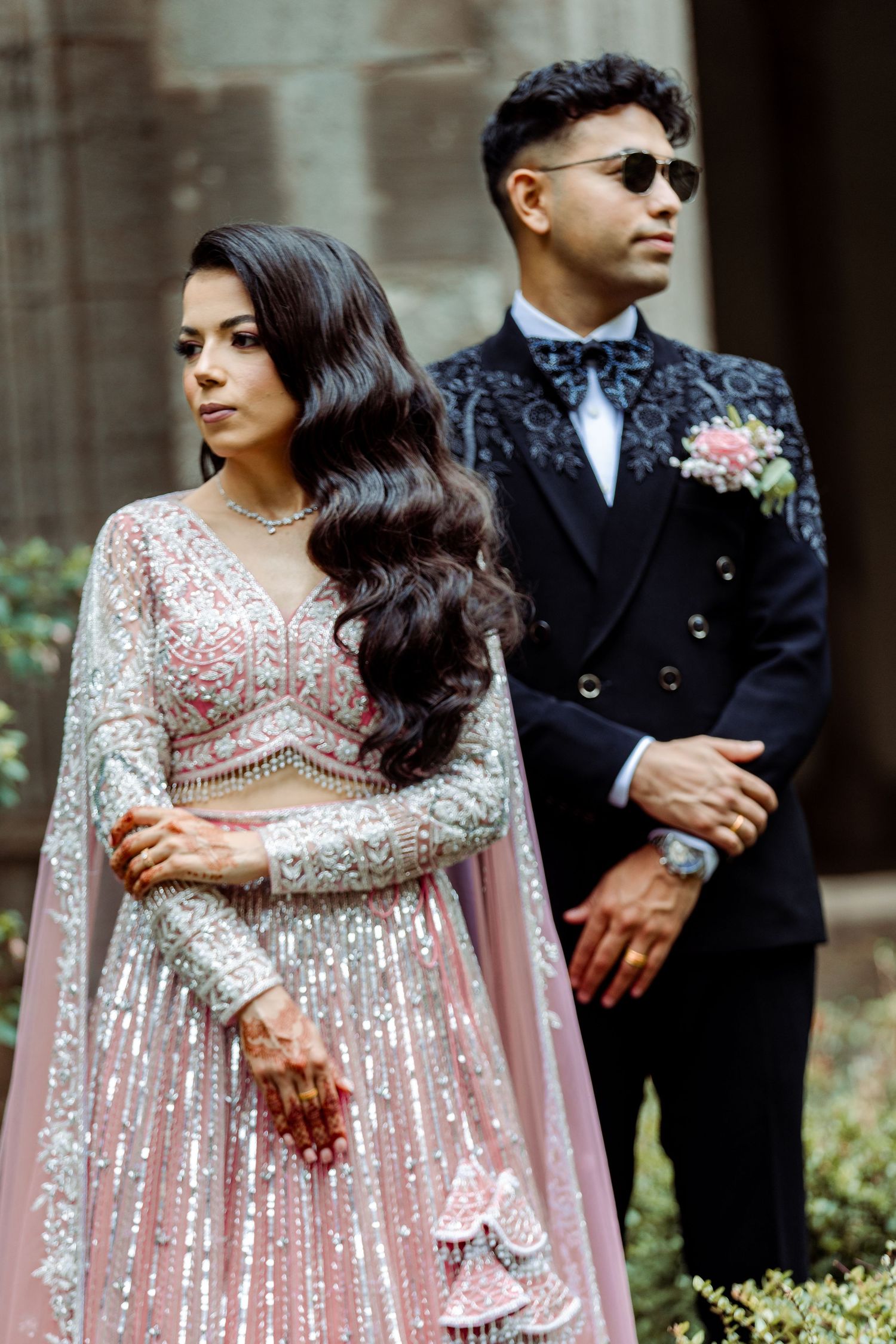 Couple in glamorous South Asian wedding attire pose for formal portrait.