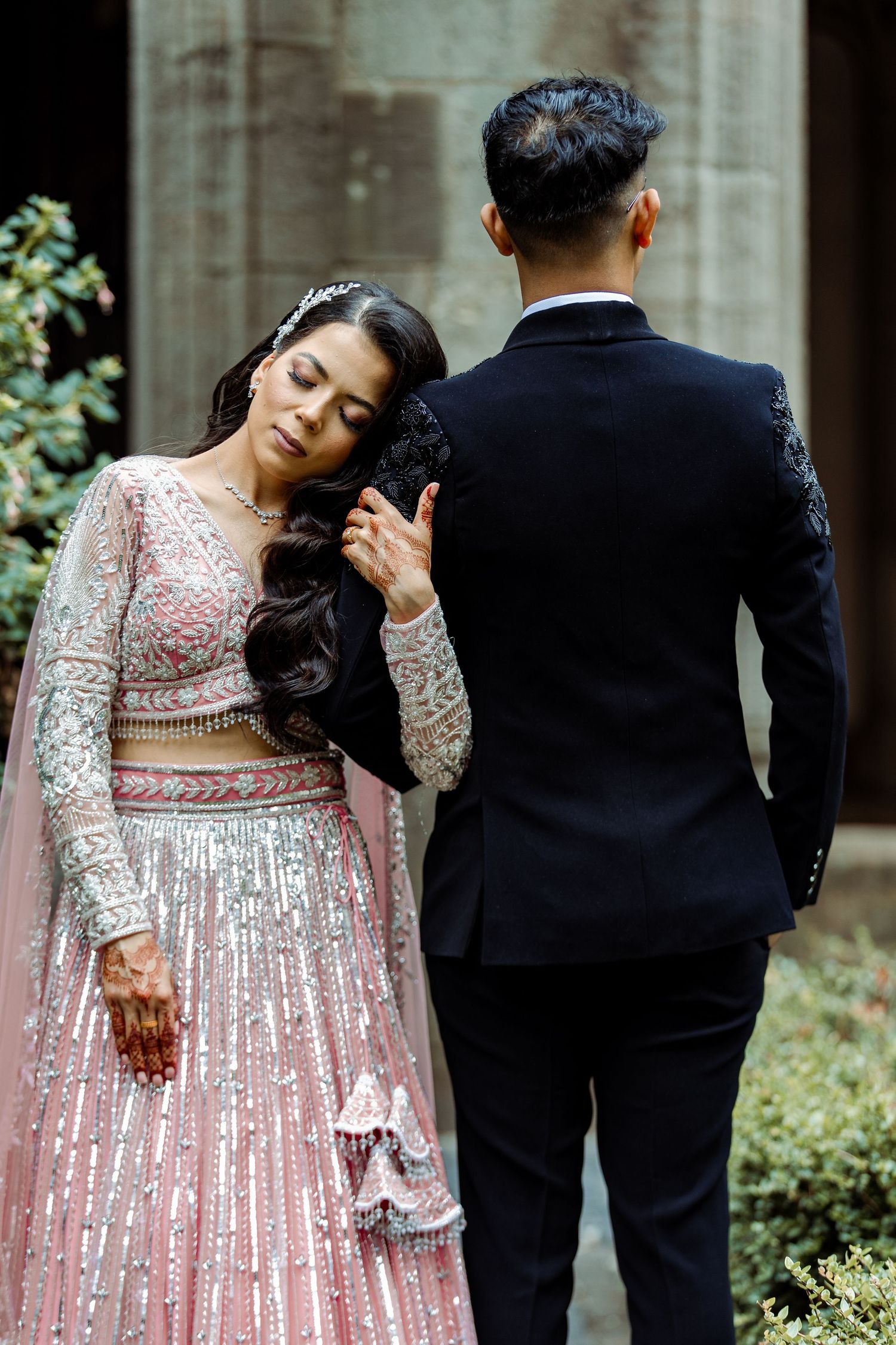 A romantic wedding portrait in front of gothic architecture with bride in pink sequined lehenga.