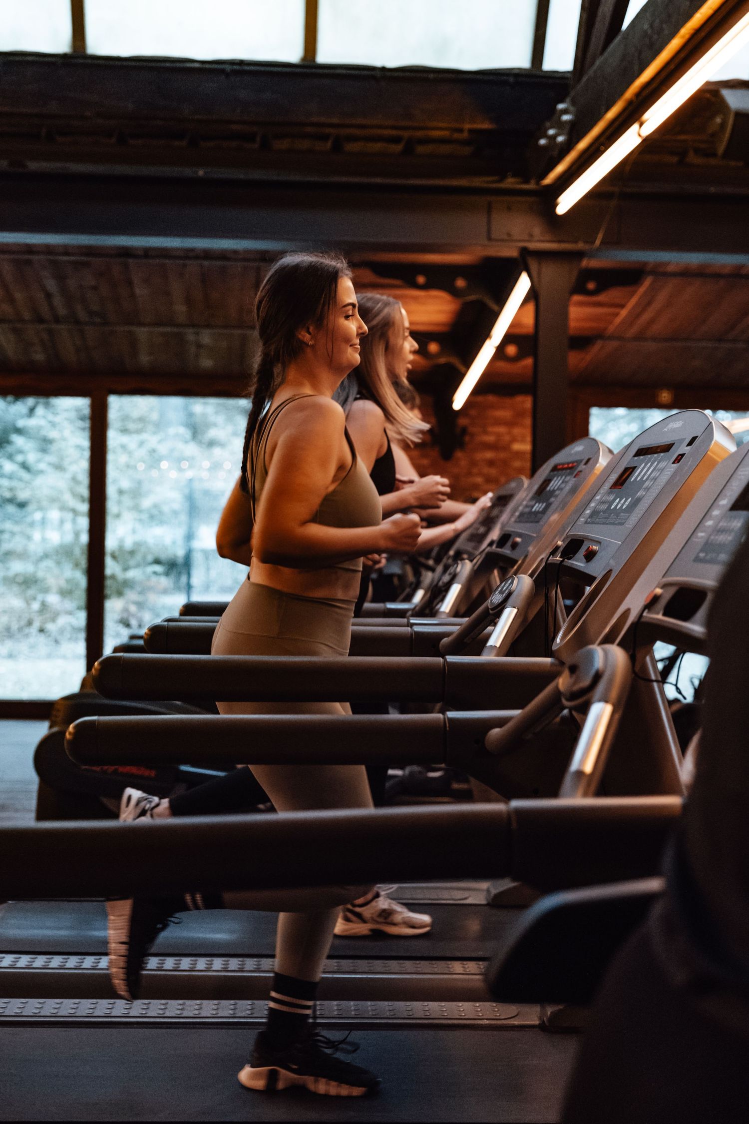 People exercising on treadmills in a modern gym with large windows.