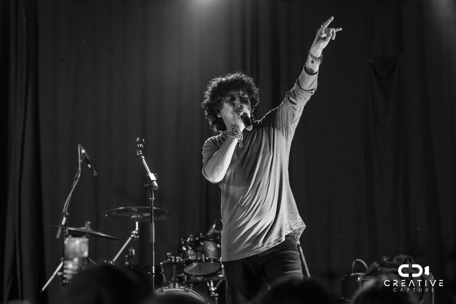 Dynamic black and white concert photo showing performer with curly hair raising arm during energetic stage performance.