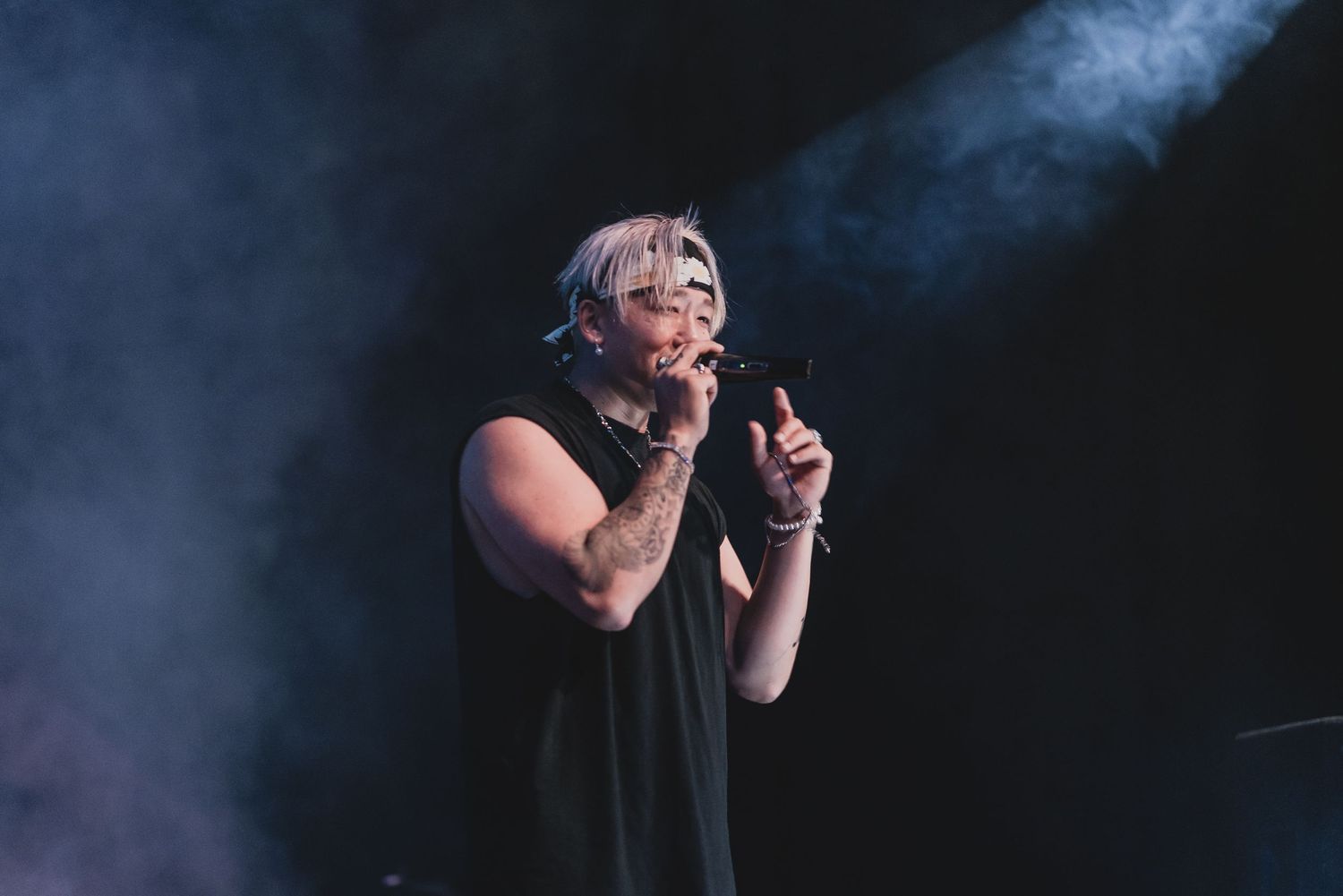 Performer in black attire singing emotionally on smoke-filled stage.