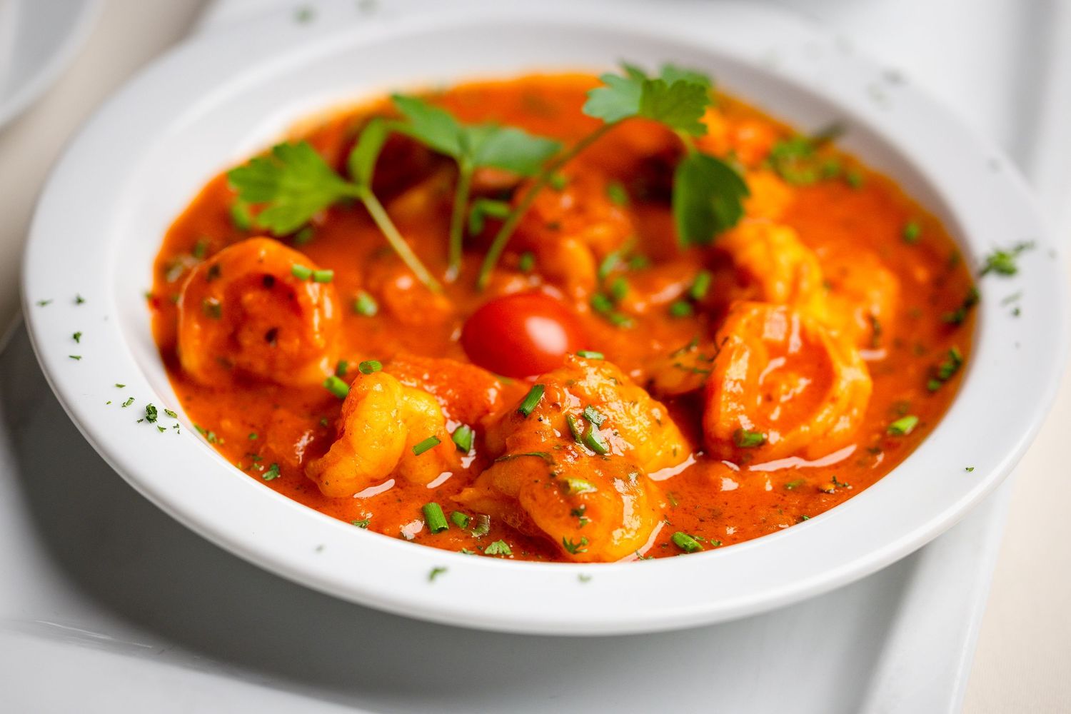 Shrimp in spicy tomato sauce garnished with fresh herbs and cherry tomatoes in white bowl.