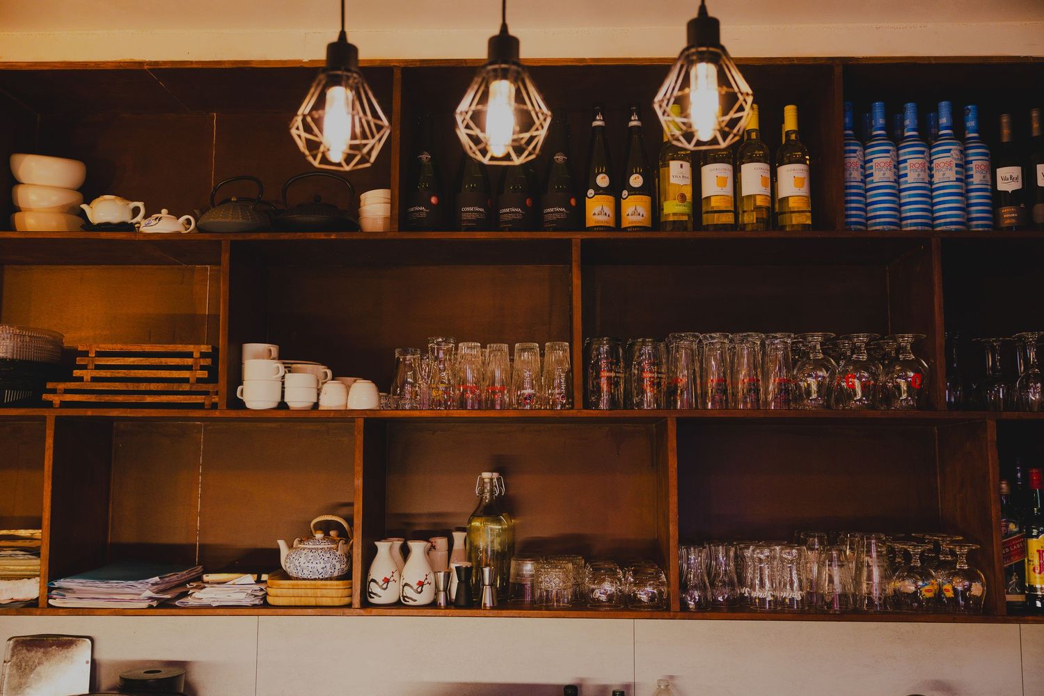 Modern bar interior with pendant lights and shelves stocked with bottles and glassware.