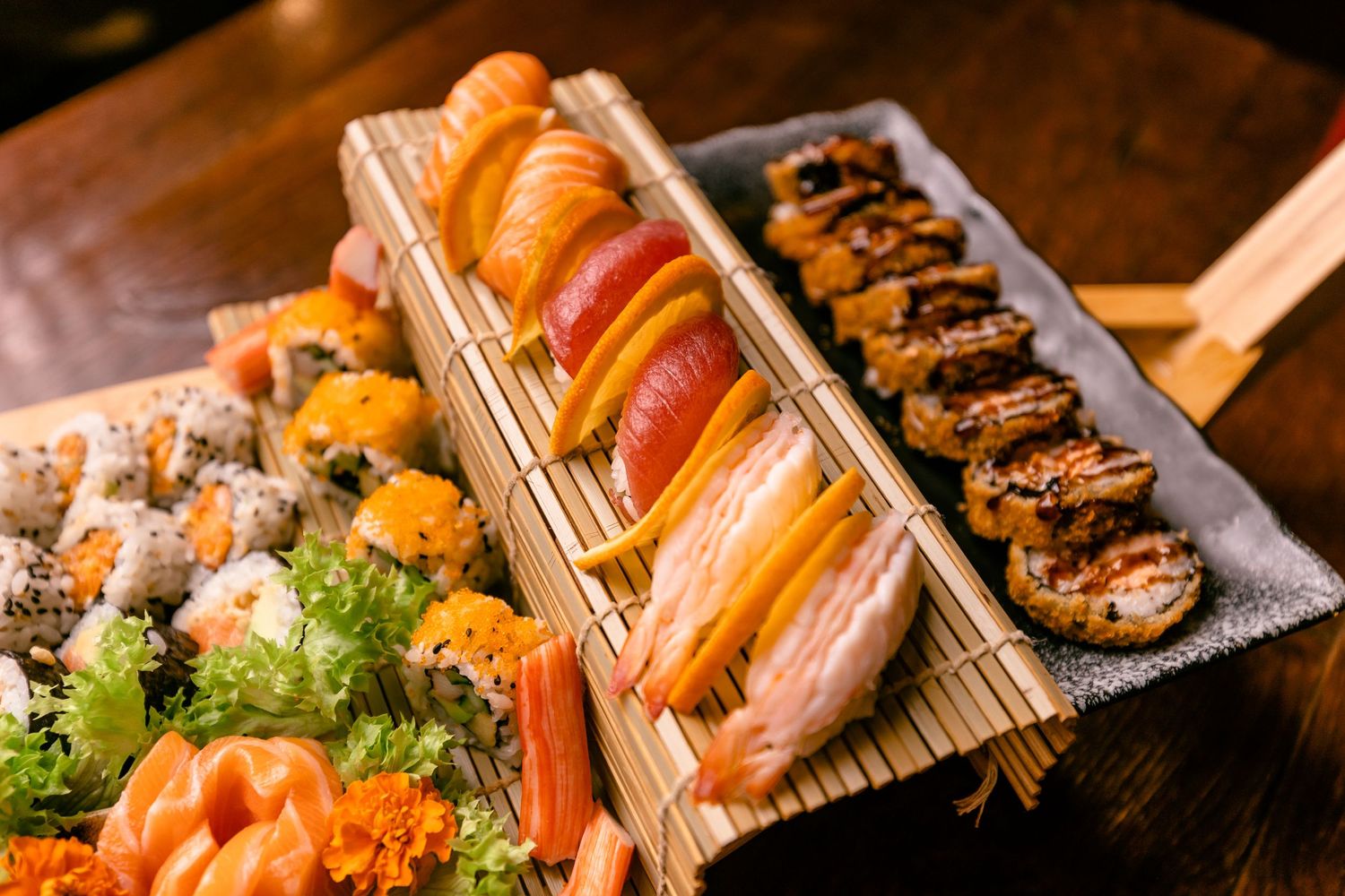 Assorted fresh sushi rolls and sashimi displayed on bamboo mats with garnishes.