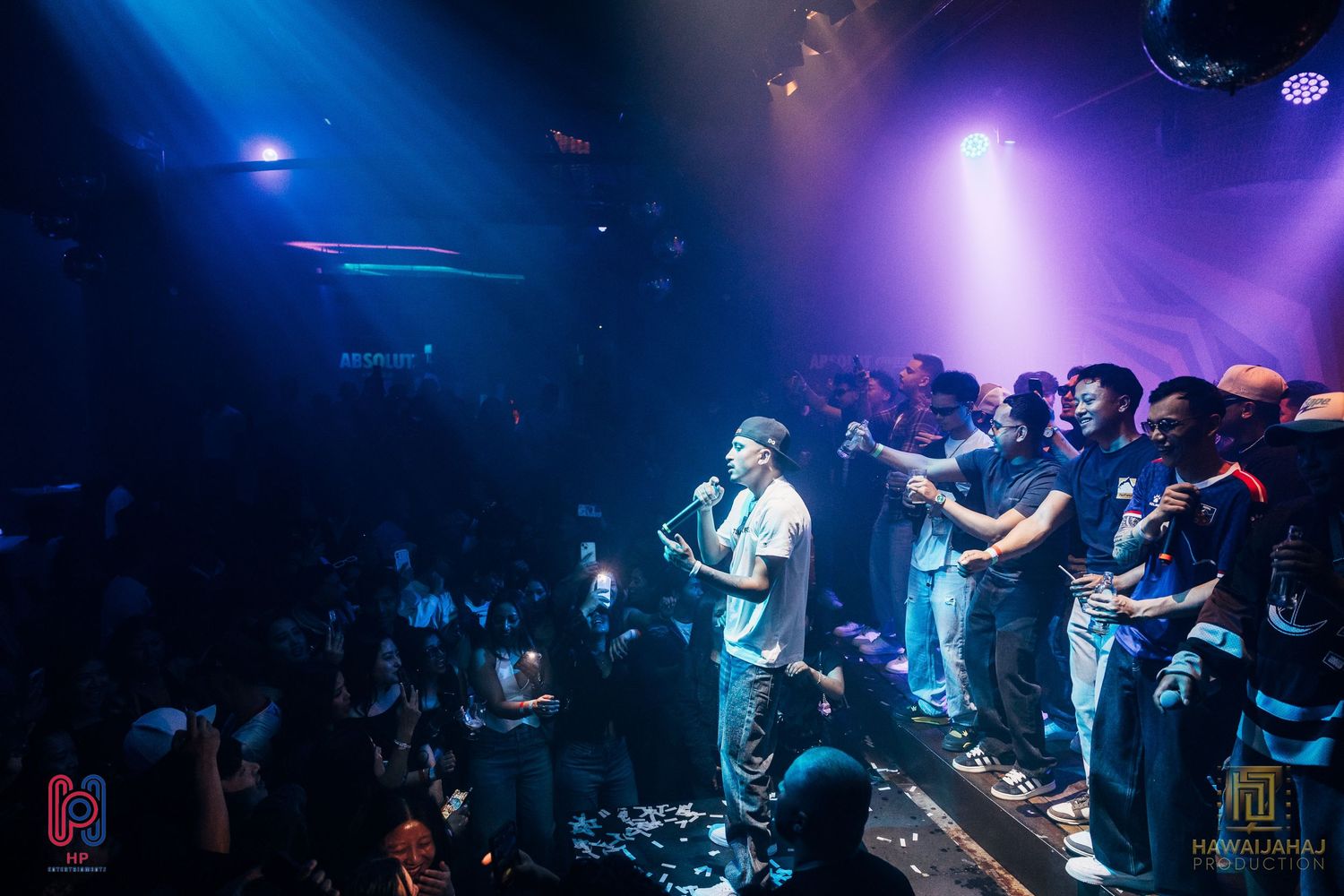 Concert crowd watching performer on stage with dramatic purple and blue lighting effects.