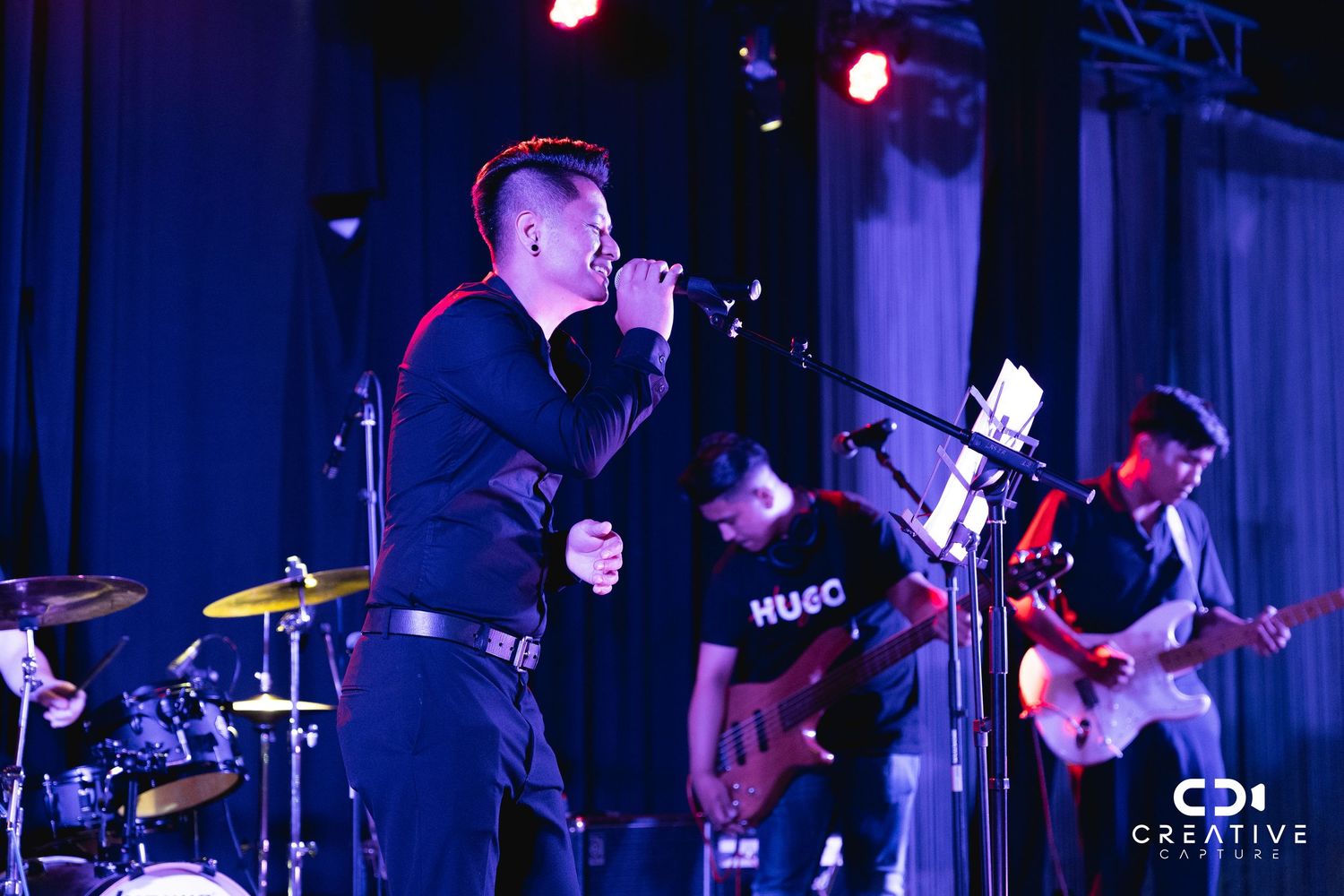 Live band performance with singer and musicians on stage under purple and blue lighting.