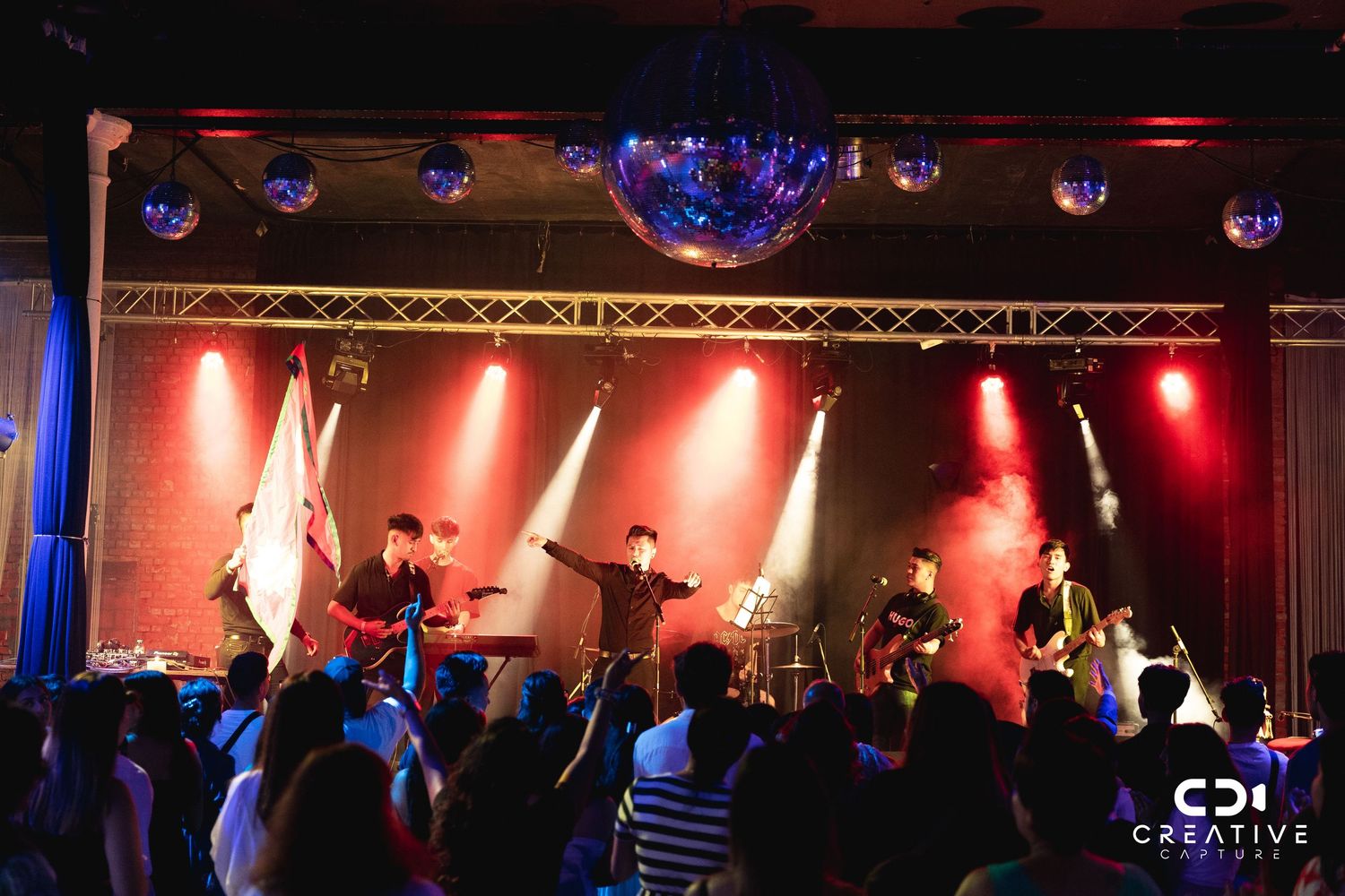 Band performing on stage with dramatic red lighting and enthusiastic crowd.
