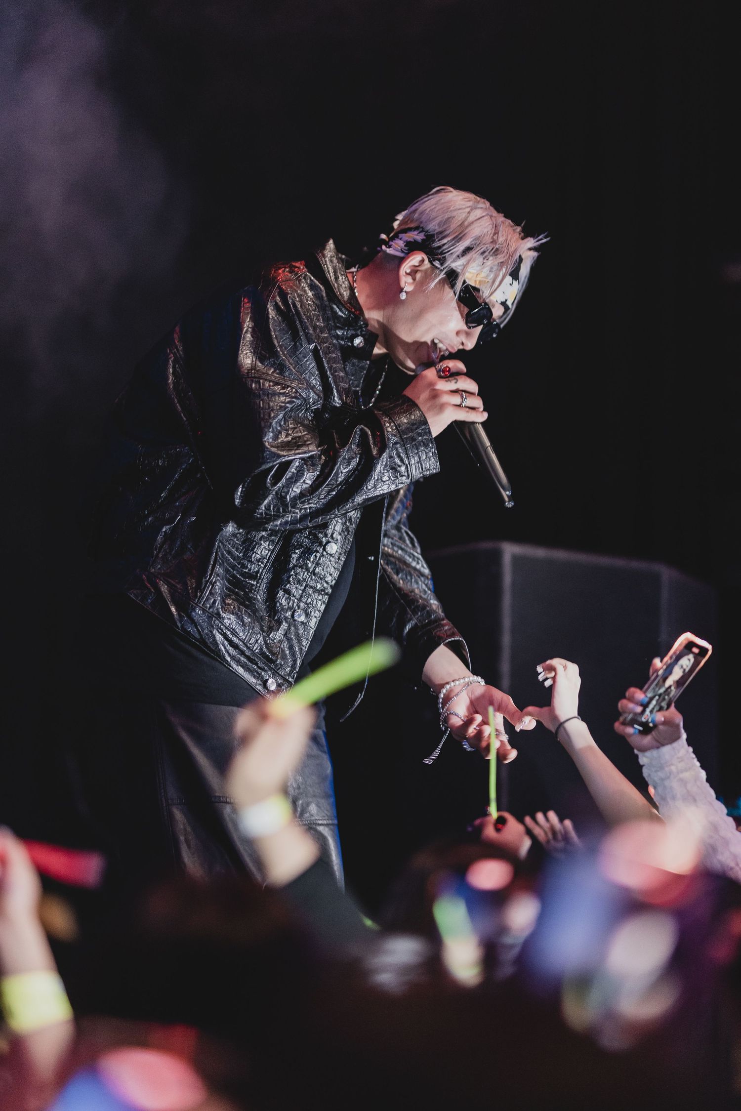 Performer in black jacket reaching toward crowd during energetic concert performance.