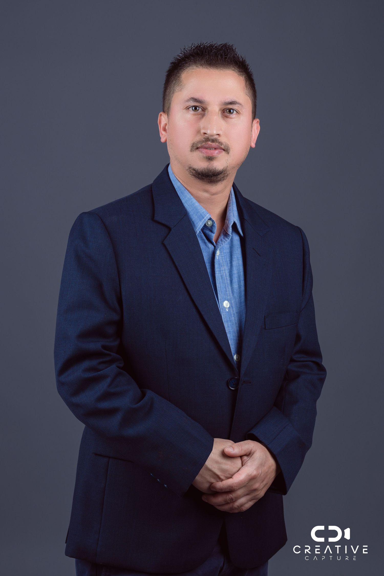 Professional business portraits in navy suit and blue shirt against grey studio background.