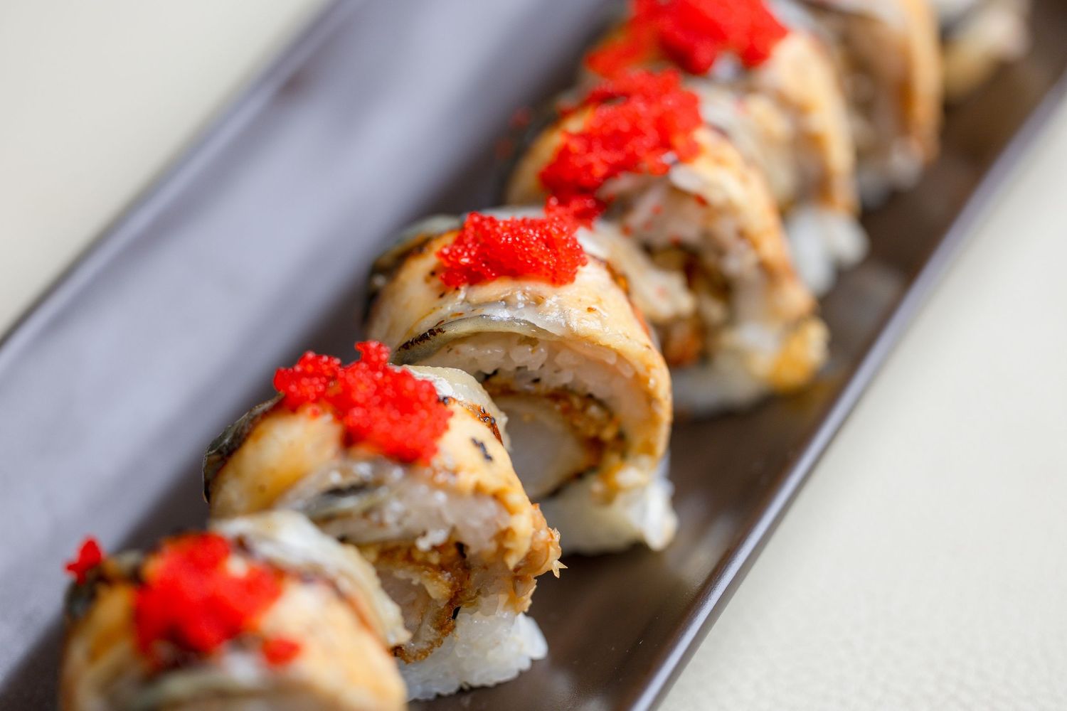 Sushi rolls topped with bright red tobiko caviar served on gray plate.