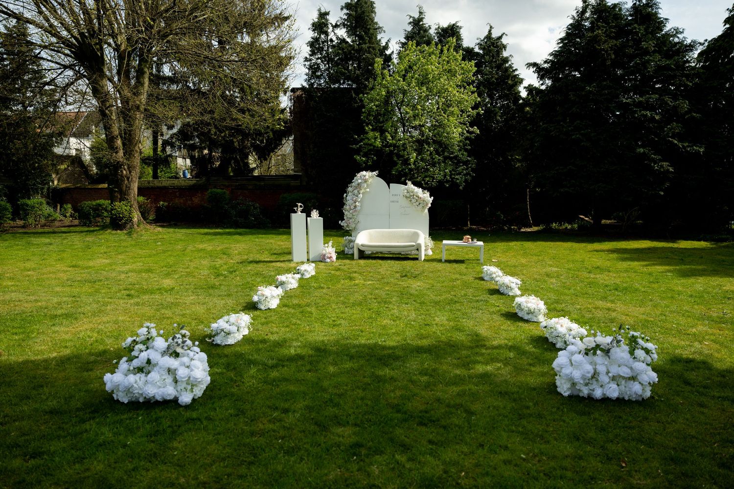 Outdoor wedding ceremony setup with white chairs and floral arrangements on green lawn.