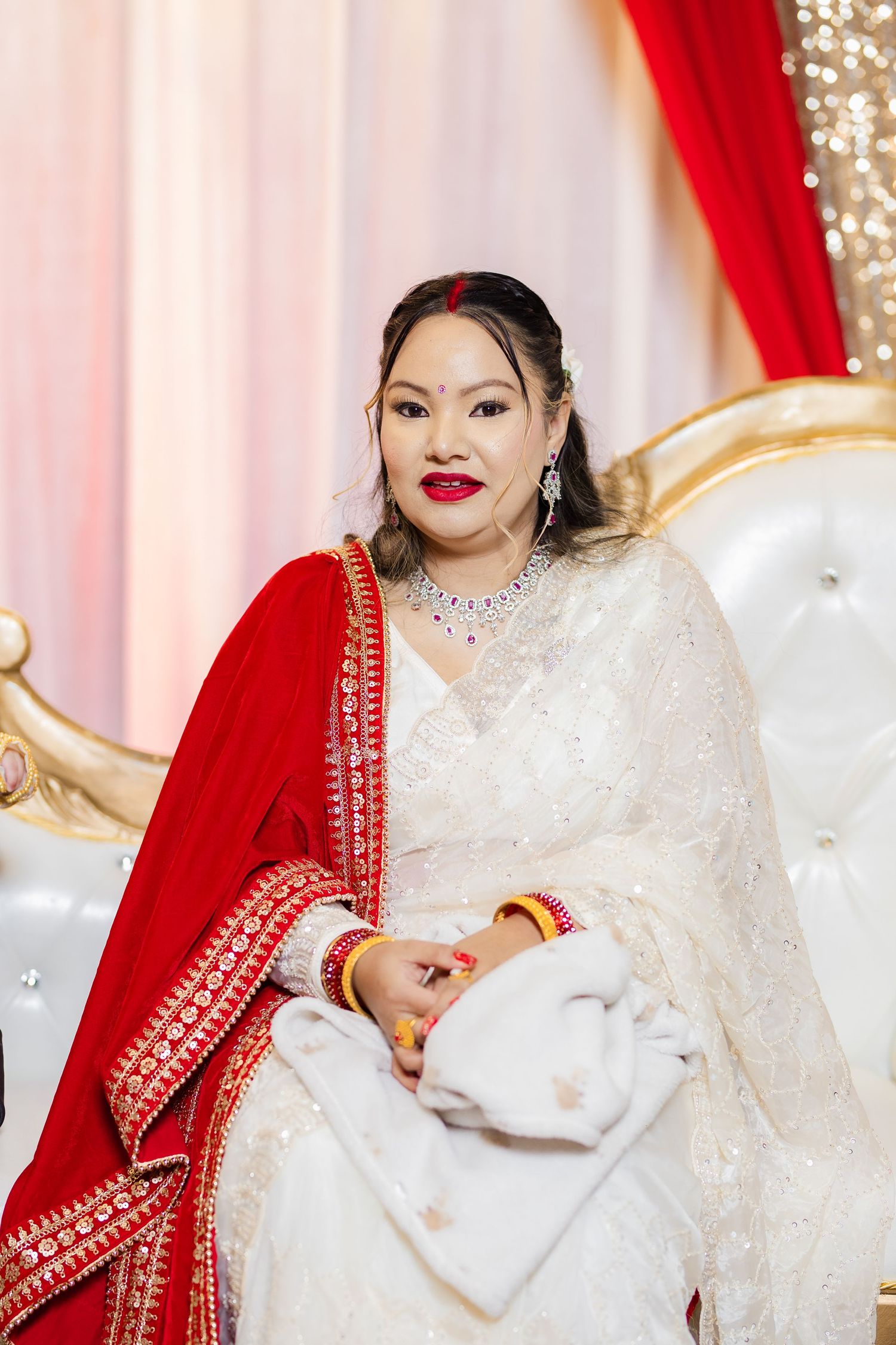 Bride in traditional South Asian wedding attire with red dupatta and white embellished dress.