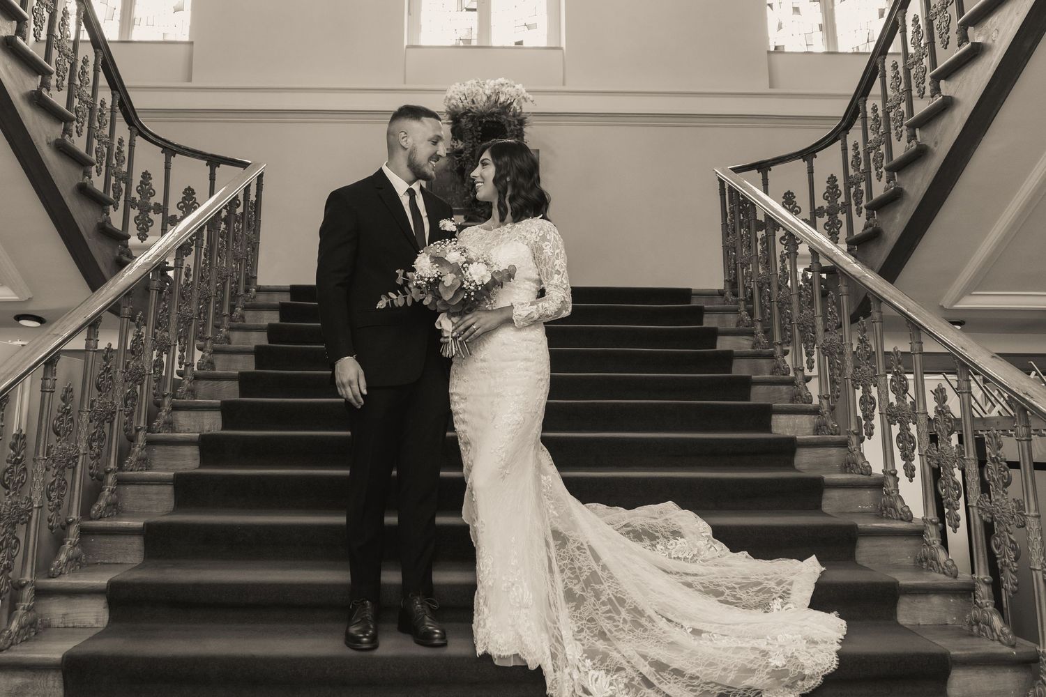 Elegant wedding couple posing on grand staircase with ornate railings.