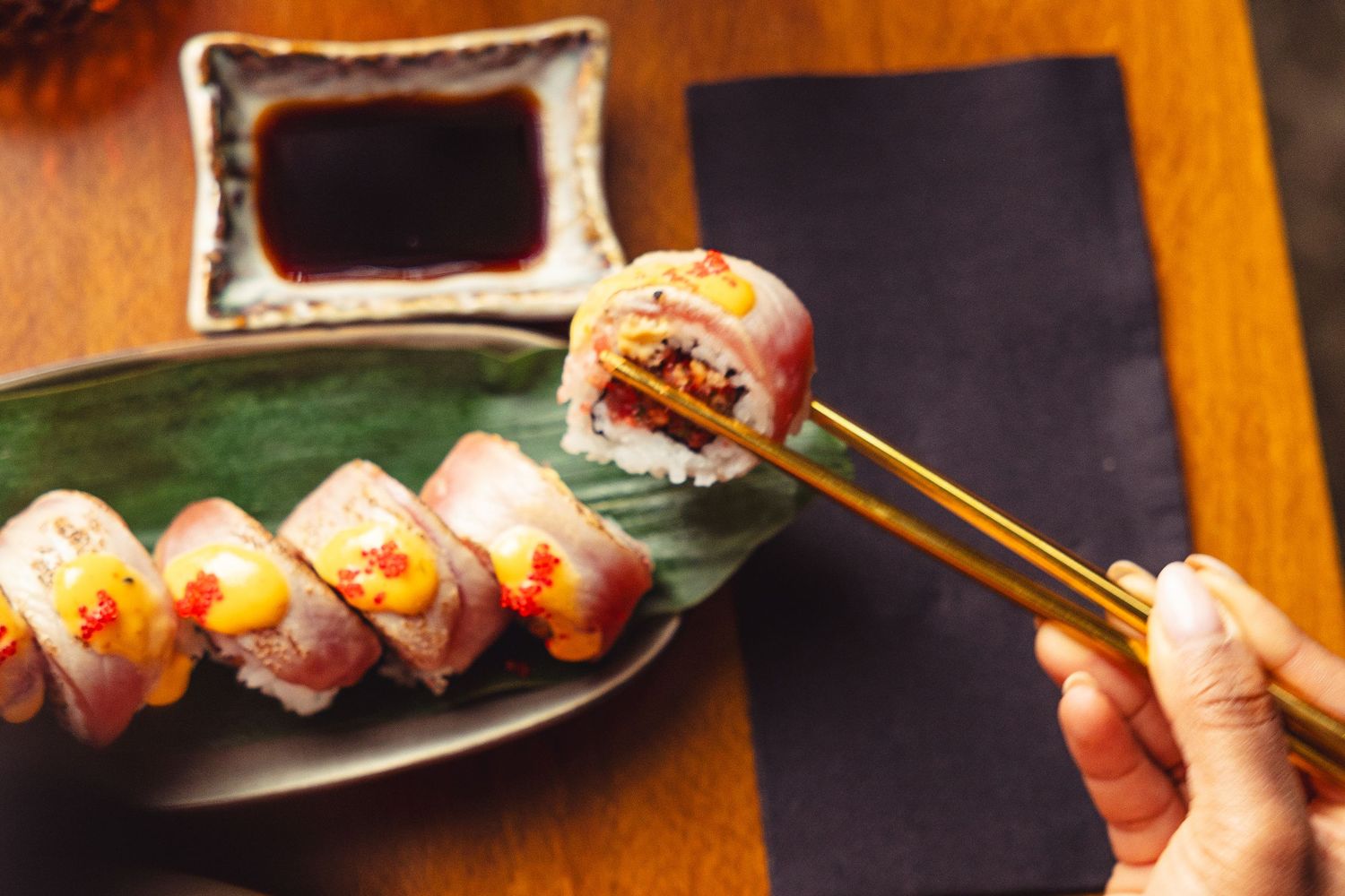 Fresh sushi rolls garnished with sauces and microgreens on dark plates.