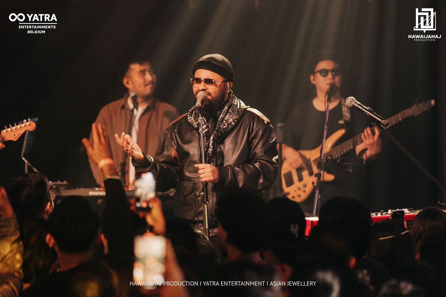Band members play instruments on a dimly lit stage during an energetic live performance.