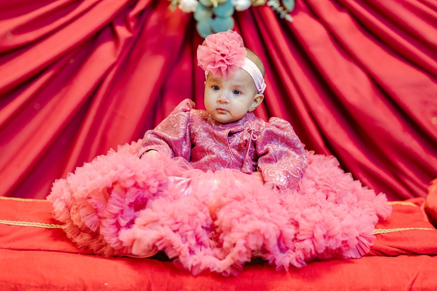Baby in pink tulle dress lying on red fabric backdrop for portrait session.