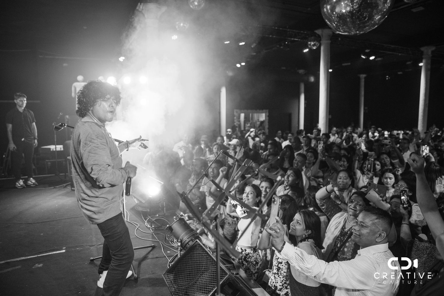 Black and white concert photo showing performer engaging with enthusiastic crowd from stage.