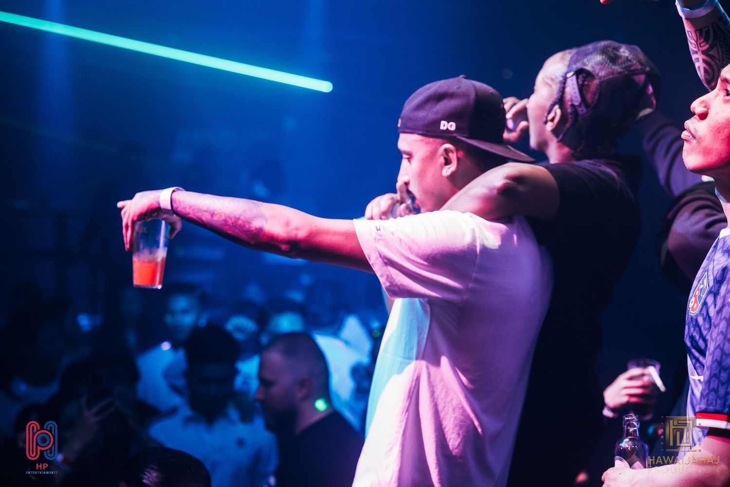 Concert attendees holding drinks and enjoying music under blue lighting at nightclub event.