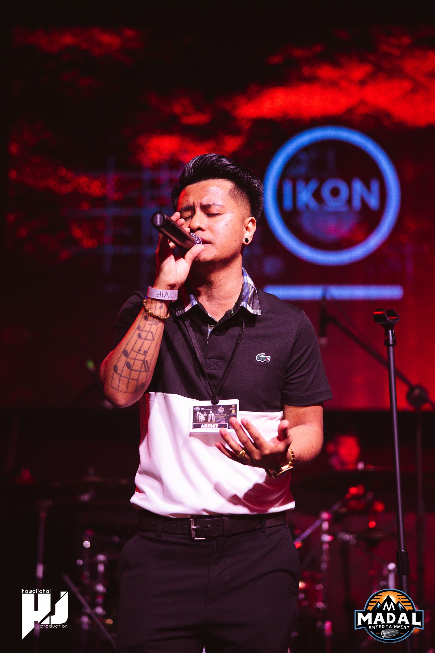 Performer singing on stage with red lighting and blue IKON logo in background during live concert performance.