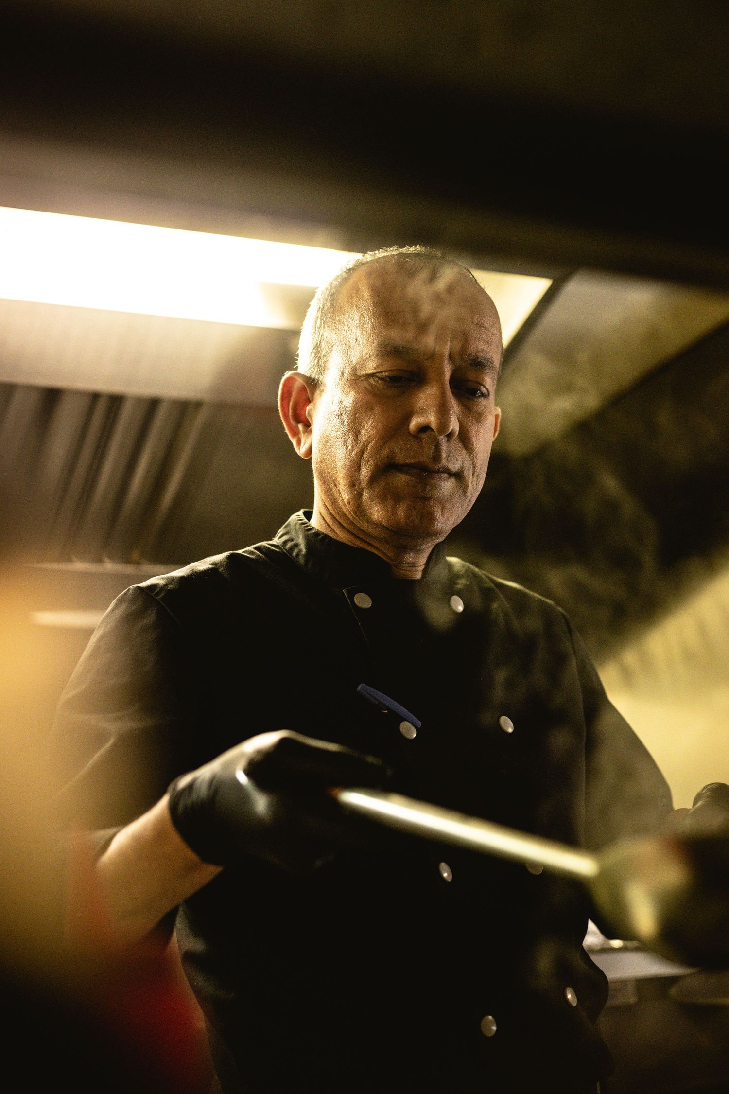 Chef in black uniform working in dimly lit professional kitchen.
