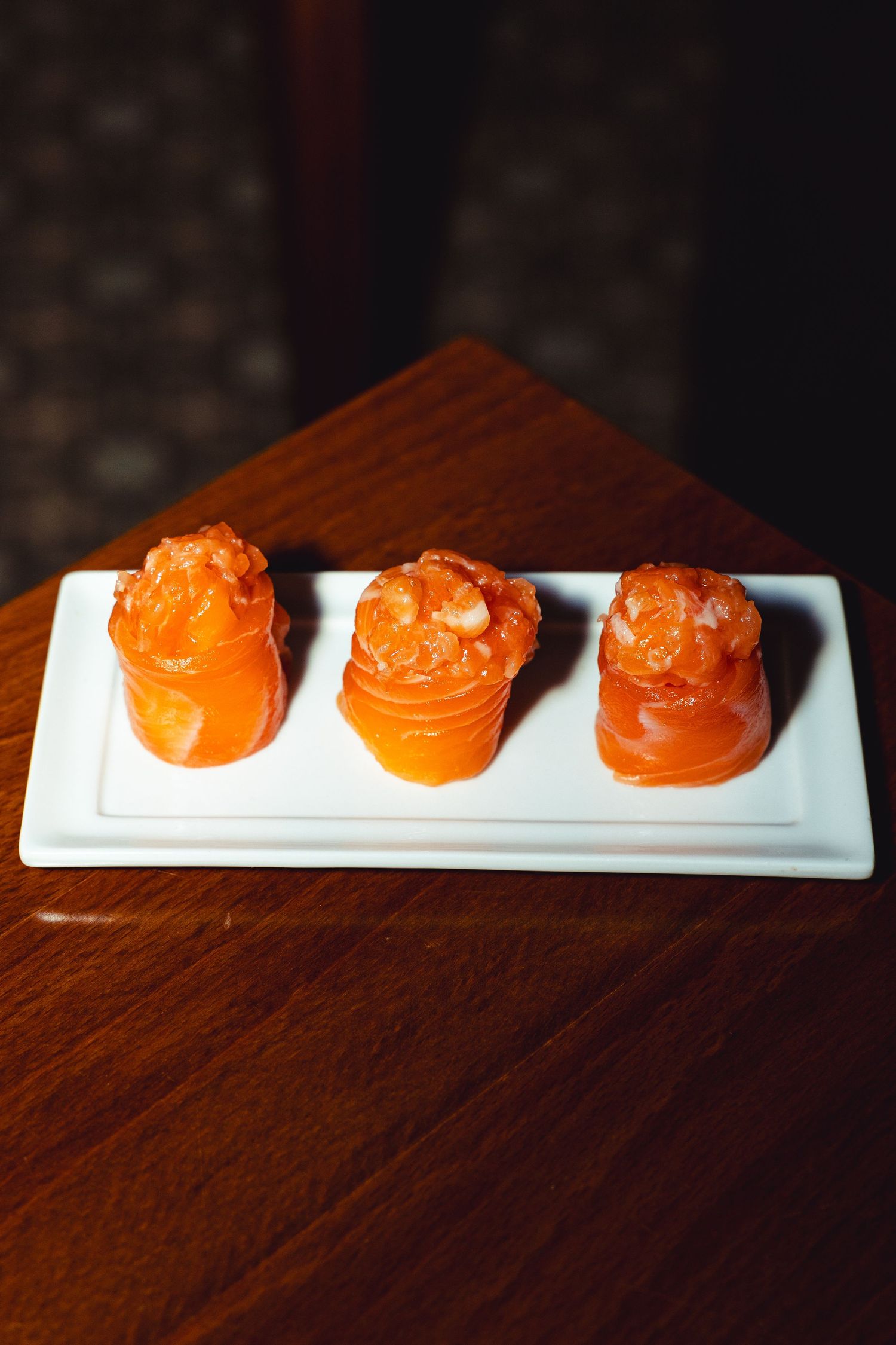 Three orange-colored sushi pieces artfully presented on white rectangular plate.