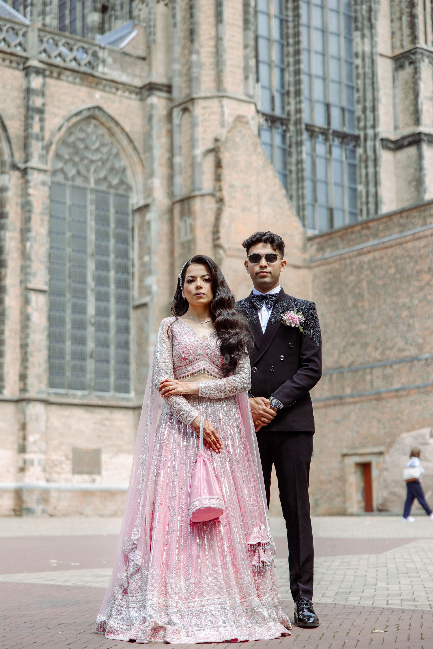Wedding couple in pink and black attire poses by gothic church exterior.
