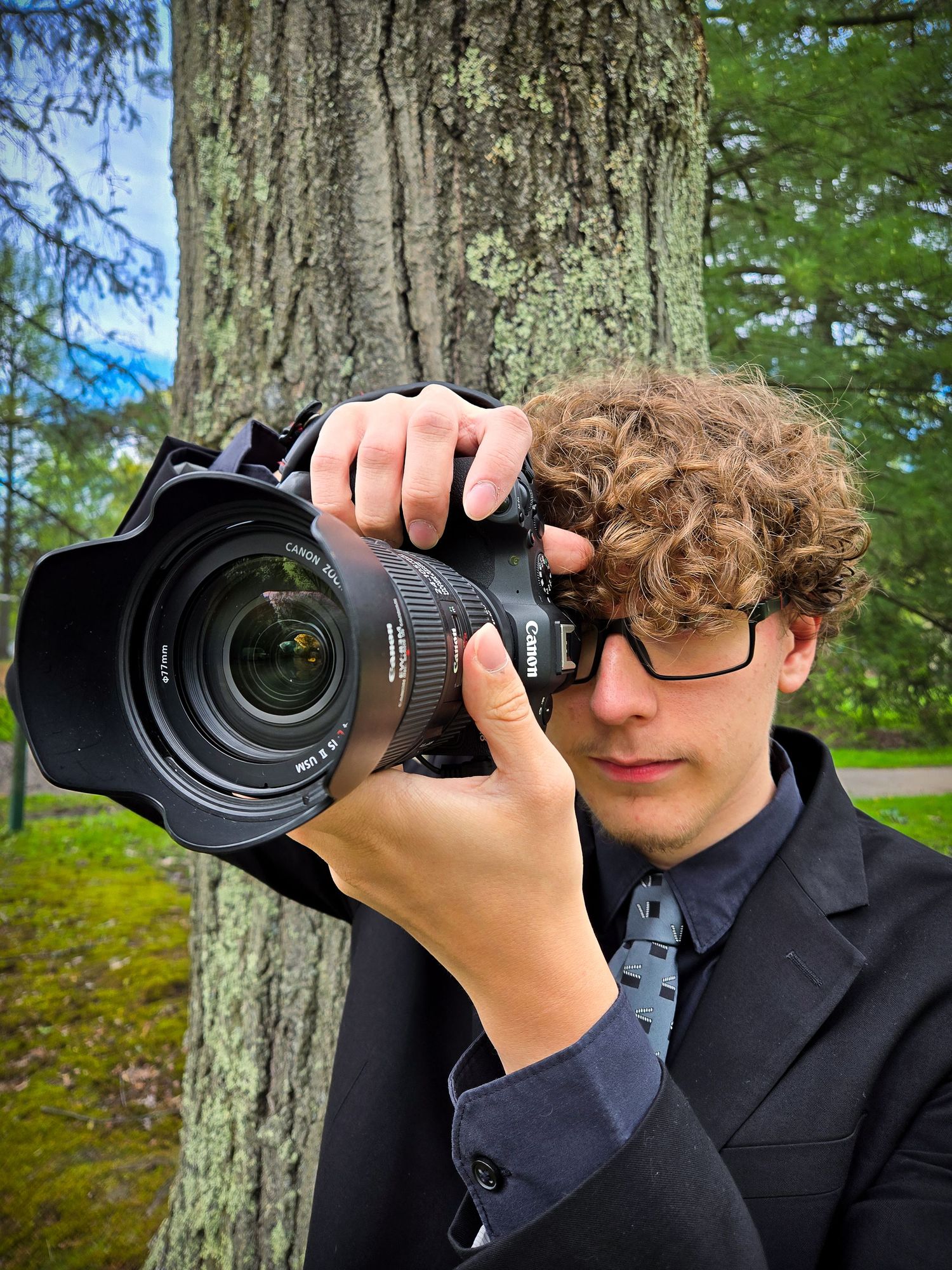 Photographer using professional camera equipment against tree trunk background.