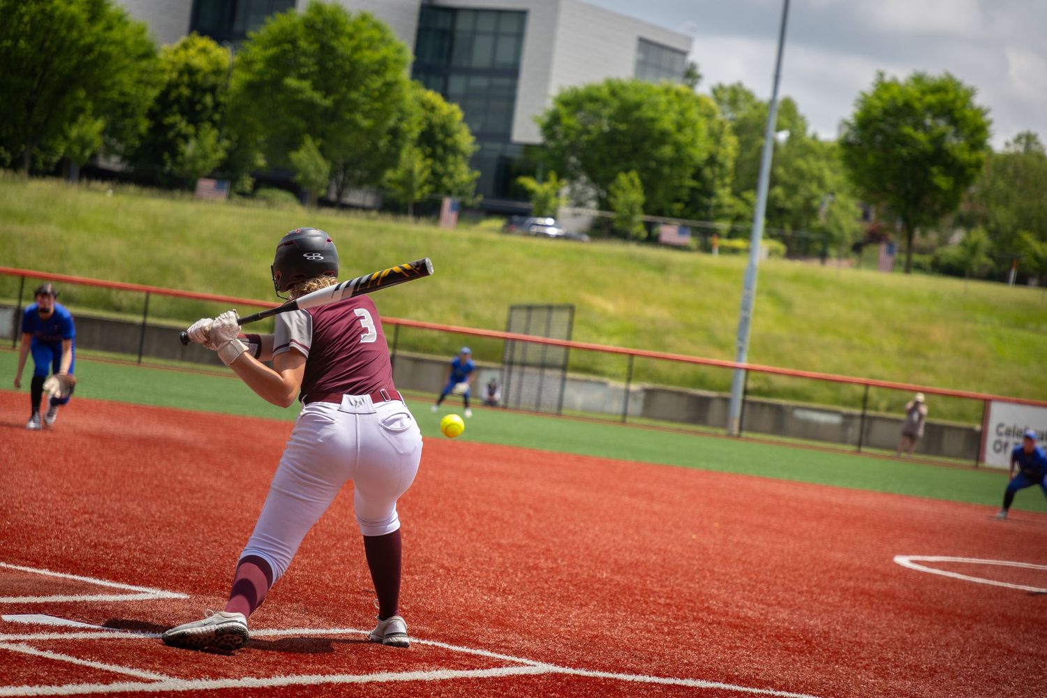 Softball player sliding into base on red clay infield during game.