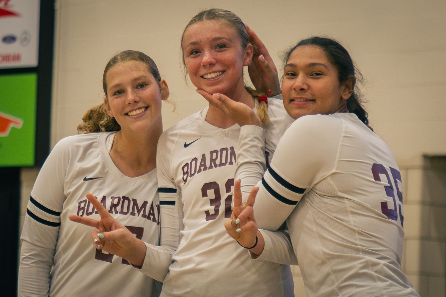Volleyball team celebrates victory with hand gestures in white uniforms.