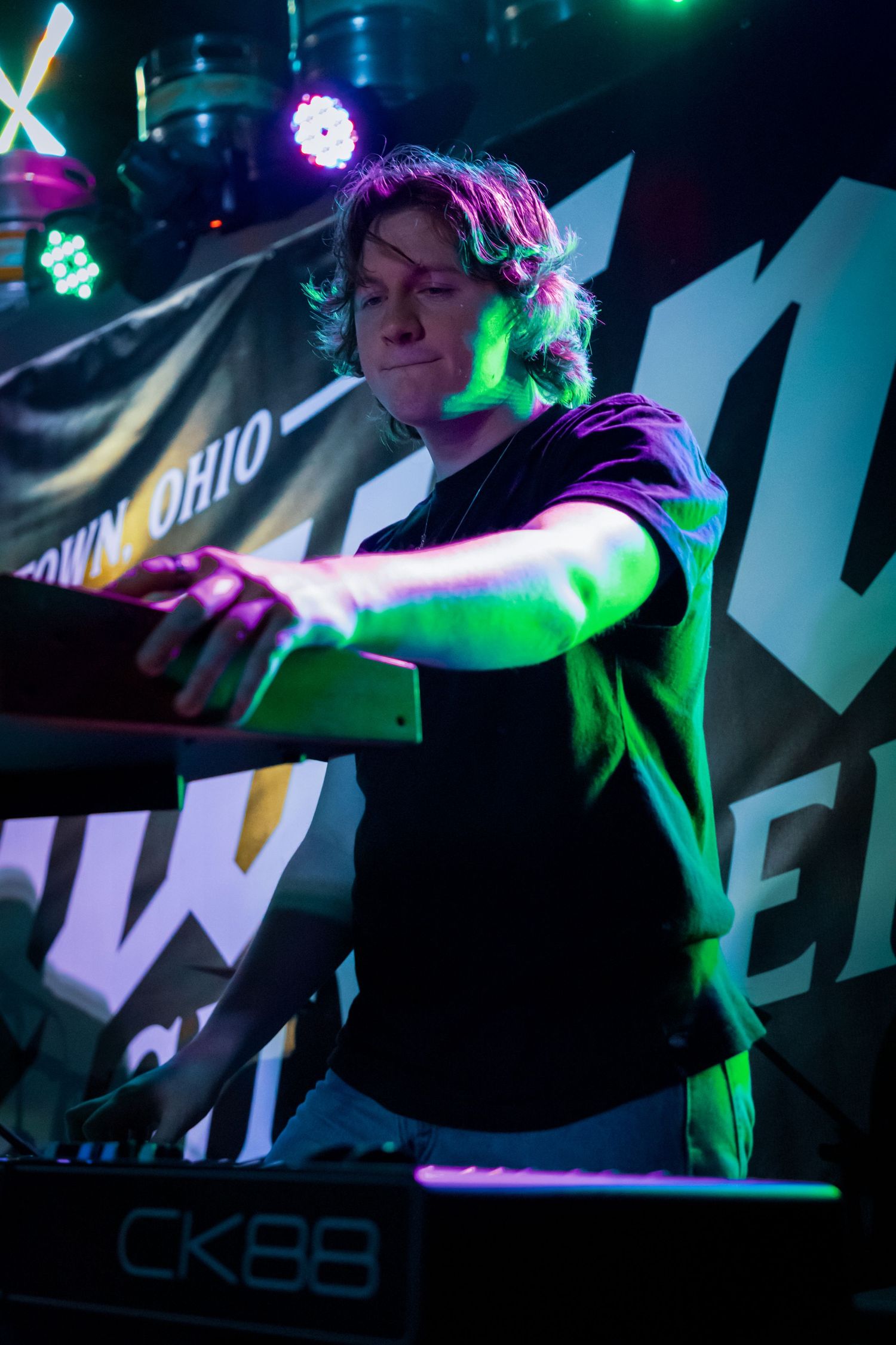 DJ equipment and controllers illuminated by green and blue stage lights during performance.