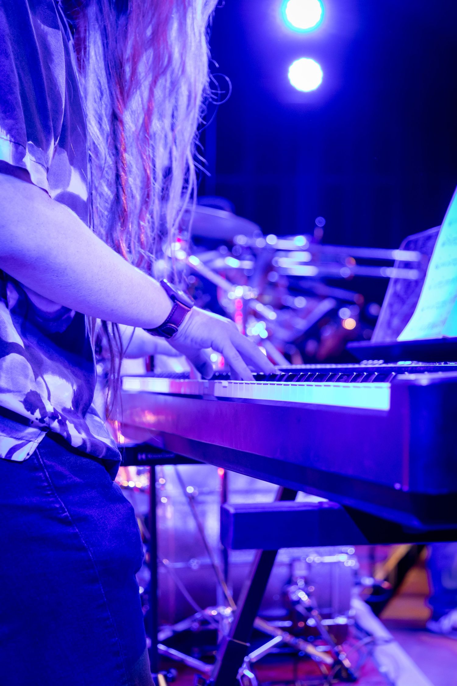 Musician with long dreadlocks playing electronic keyboard on stage under purple concert lights.