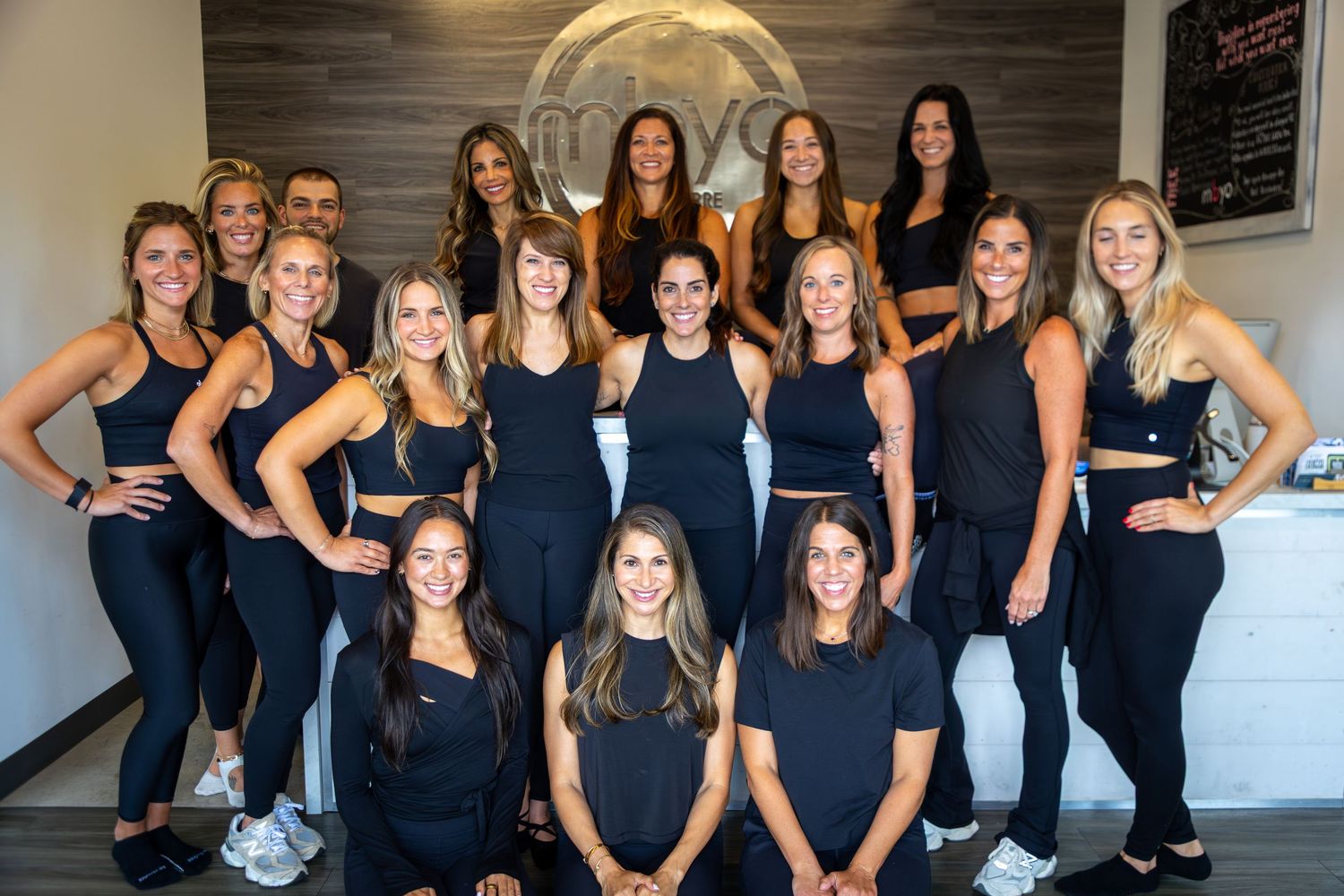 Group photo of fitness instructors wearing matching black outfits in a studio setting.