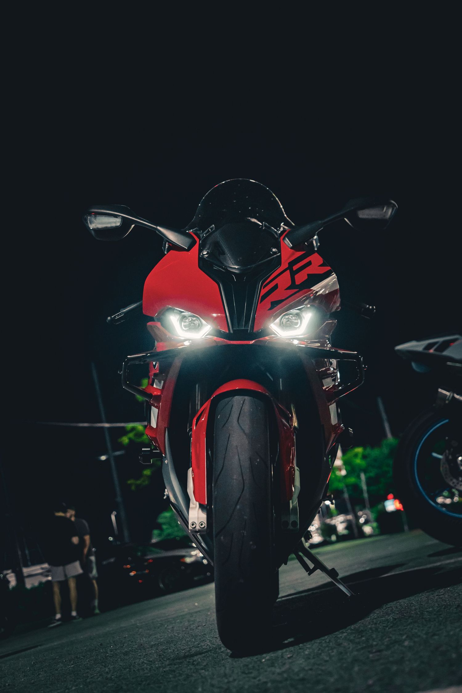 Red sport motorcycle with bright LED headlights parked on a dark street at night, front view.