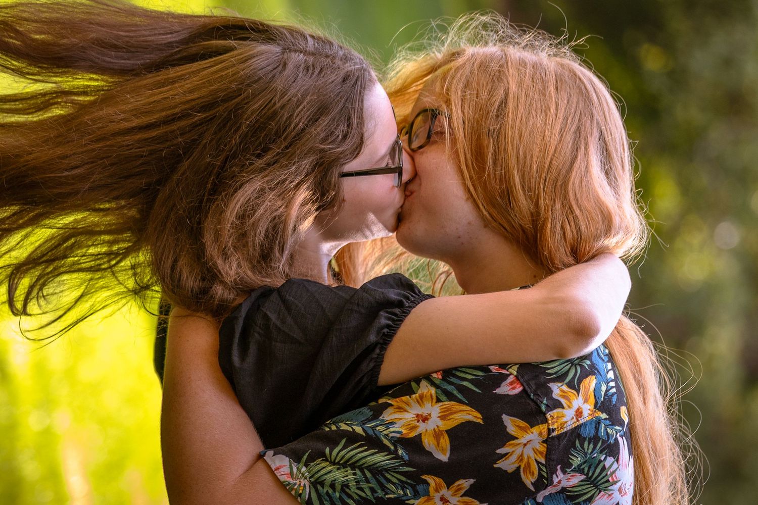 Two people share an intimate moment outdoors in a park with golden sunlight filtering through trees.
